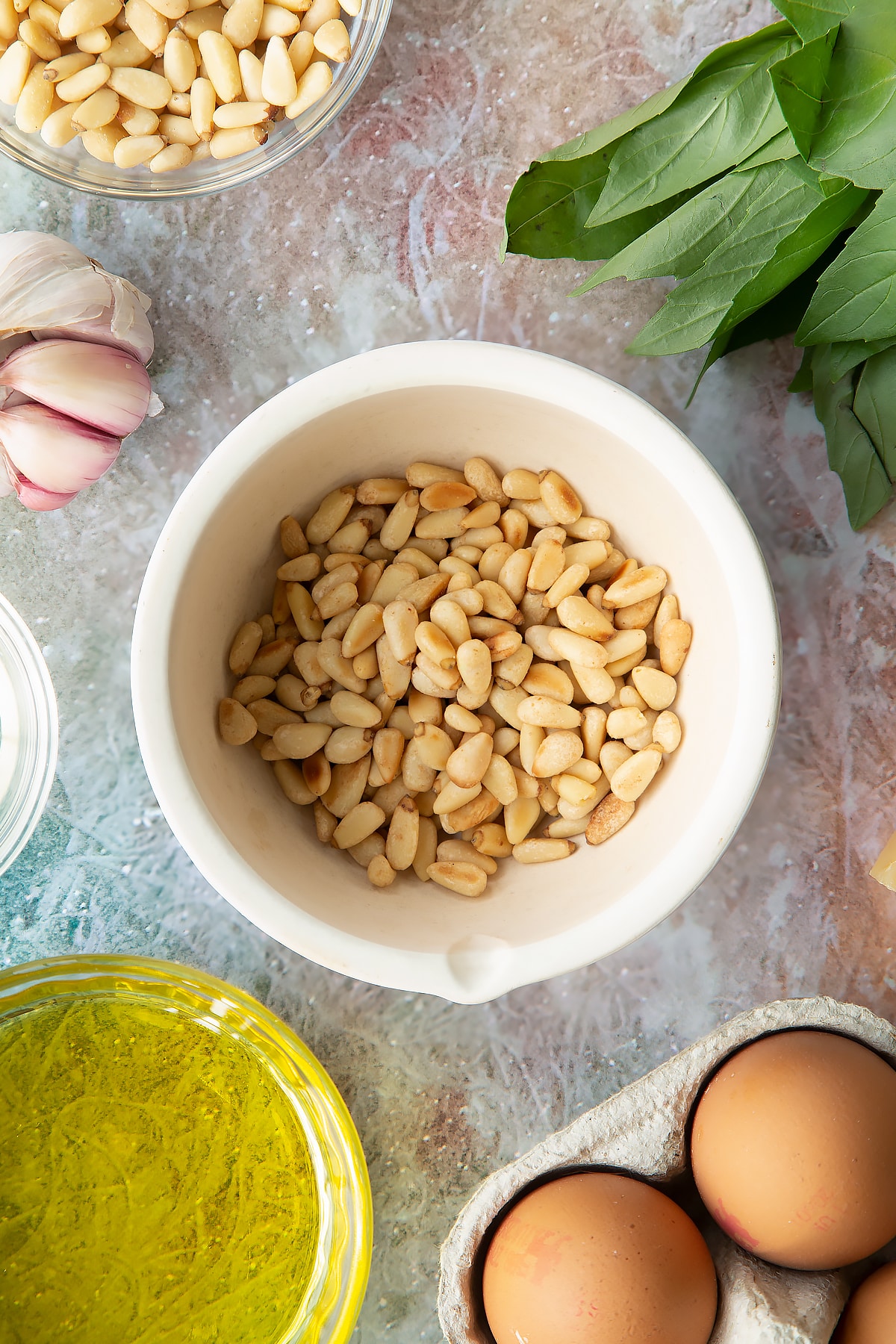 Toasted pine nuts in a small mortar. Ingredients to make pesto mayo surround the mortar.