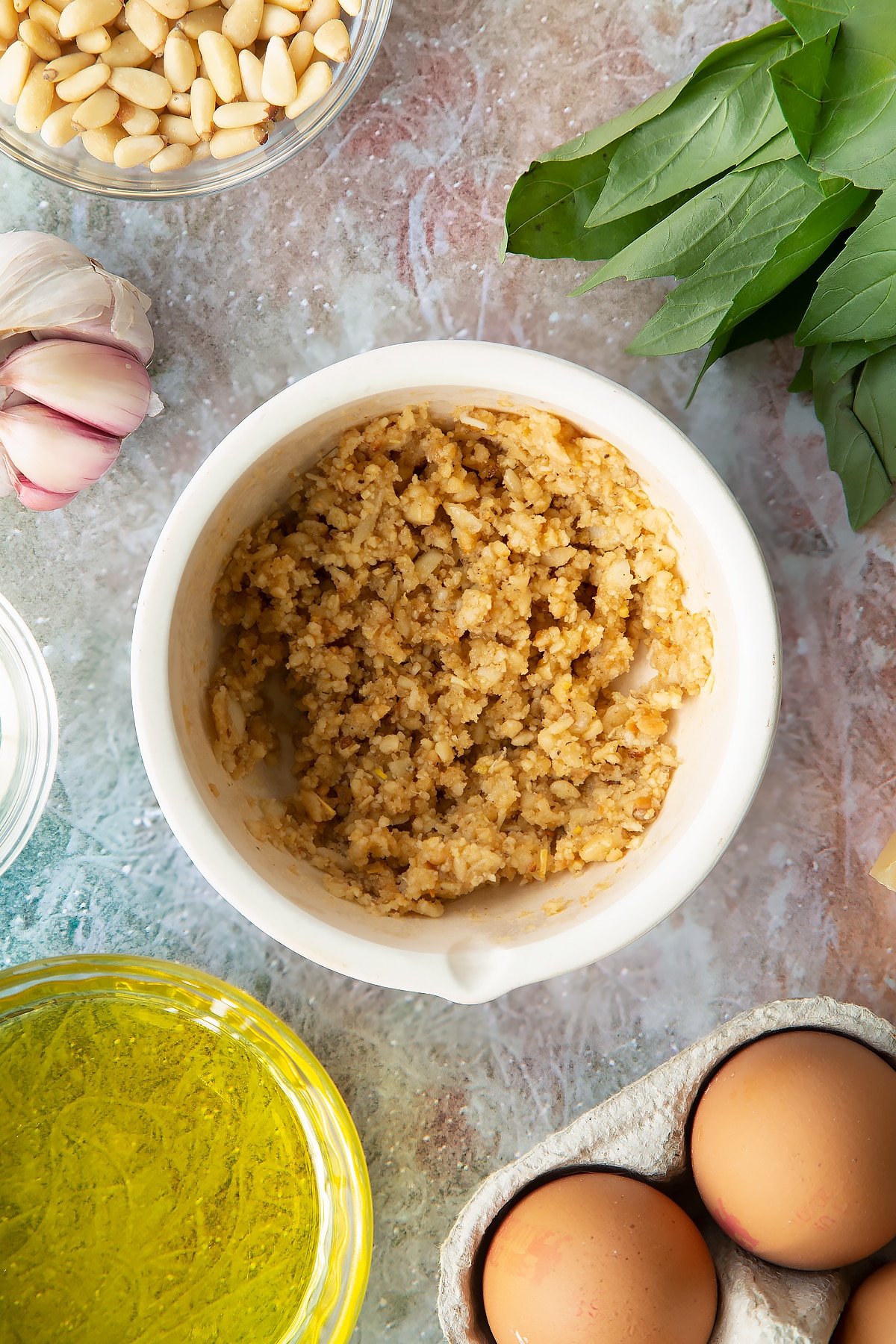Toasted pine nuts, garlic, salt and pepper crushed in a small mortar. Ingredients to make pesto mayo surround the mortar.