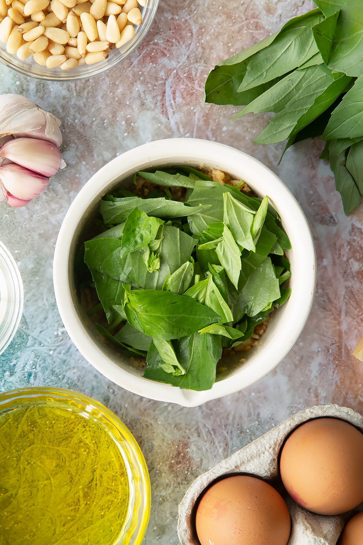 Toasted pine nuts, garlic, salt and pepper crushed in a small mortar with basil on top. Ingredients to make pesto mayo surround the mortar.