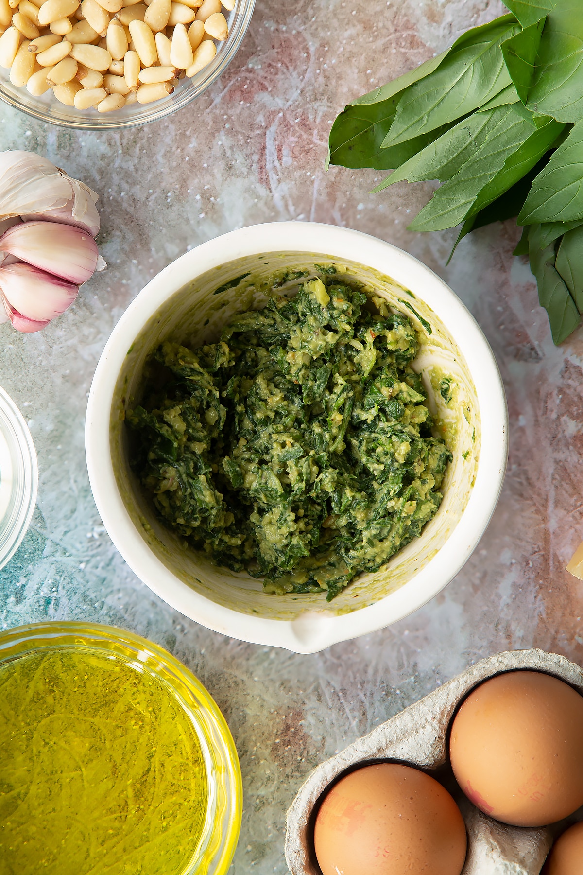 Toasted pine nuts, garlic, basil, salt and pepper crushed in a small mortar. Ingredients to make pesto mayo surround the mortar.