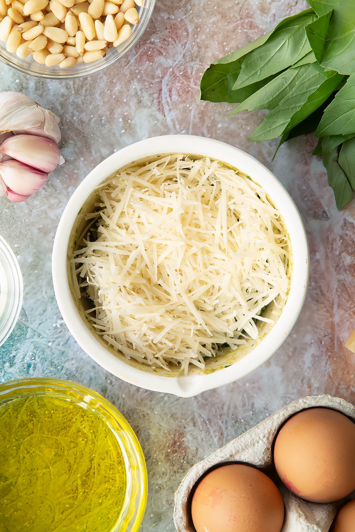 Toasted pine nuts, garlic, basil, salt and pepper crushed in a small mortar with Parmesan and olive oil on top. Ingredients to make pesto mayo surround the mortar.