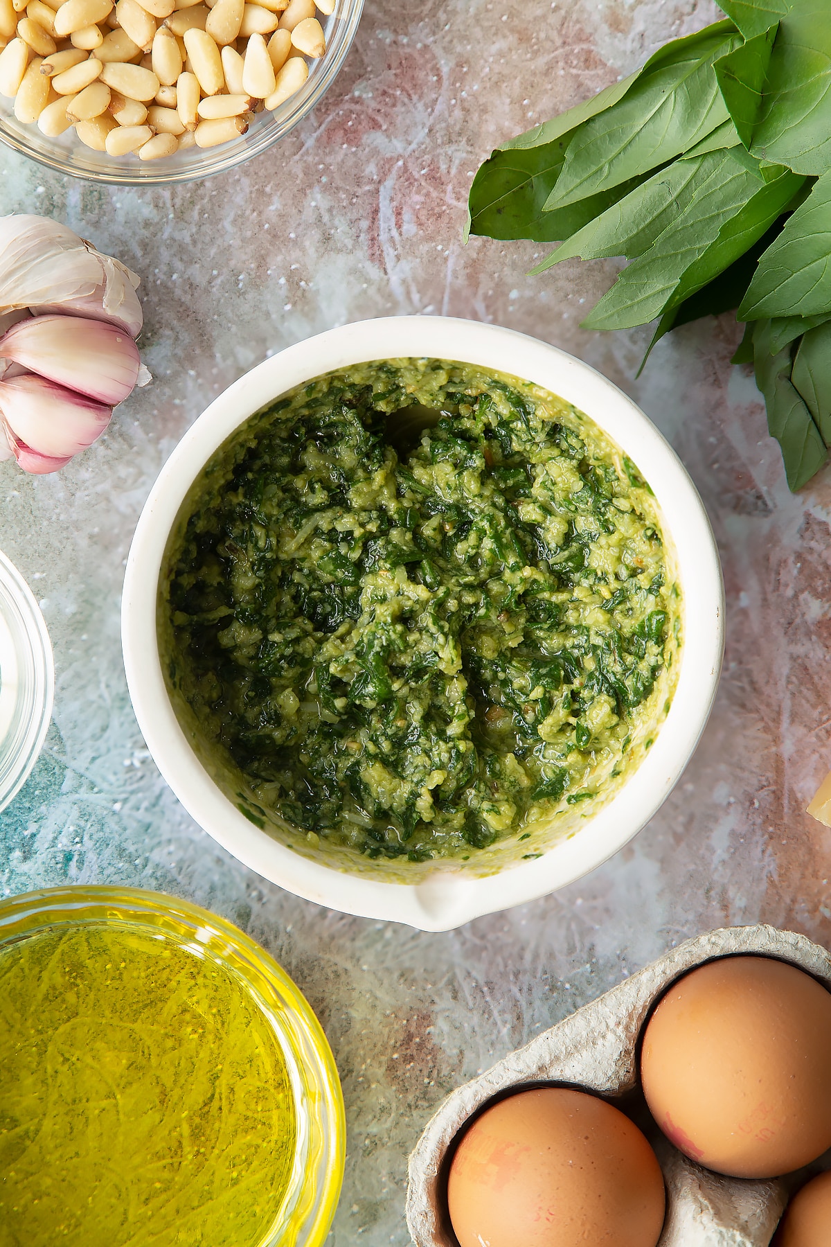 Pesto in a small mortar. Ingredients to make pesto mayo surround the mortar.
