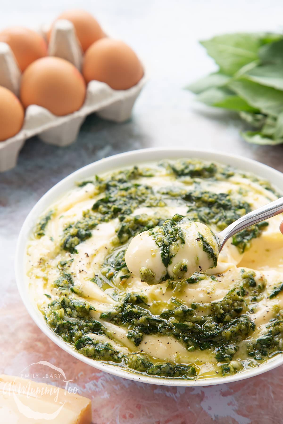Pesto mayo in a white bowl. The pesto and mayonnaise are swirled together. A spoonful hovers above the bowl.