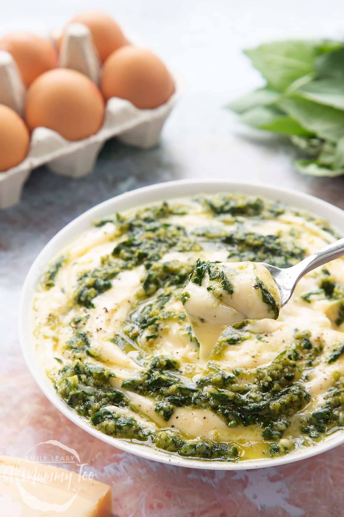 Pesto mayo in a white bowl. The pesto and mayonnaise are swirled together. A spoonful is above the bowl, which is dripping slightly