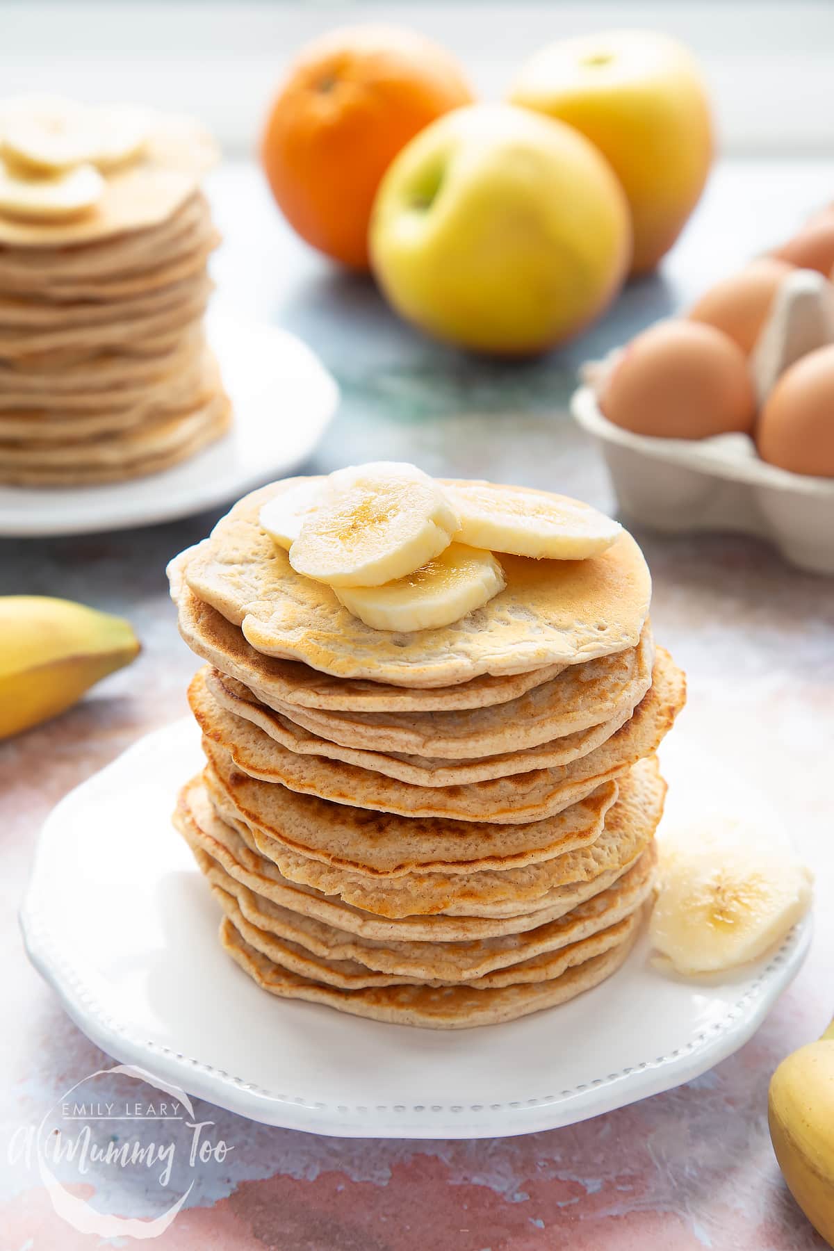 Overhead shot of a pancake stack on a white plate topped with banana with the A Mummy Too logo in the corner