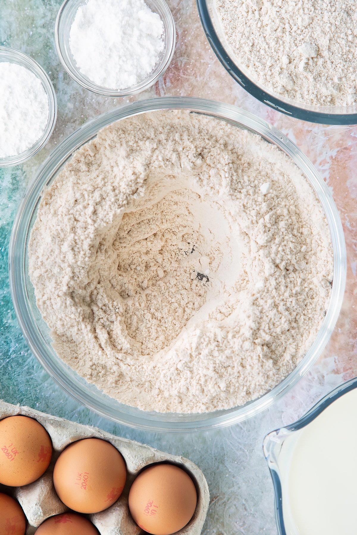 Overhead shot of flour, baking powder, icing sugar and a pinch of salt mixed in a large clear bowl