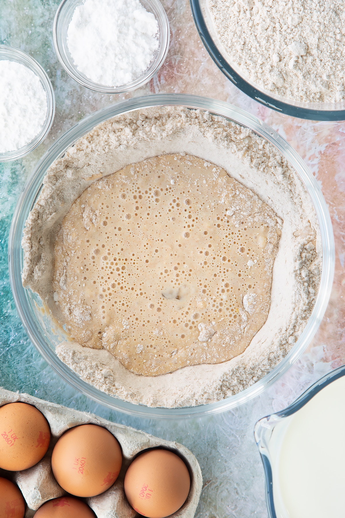Overhead shot of flour milk and eggs mixed in a large clear bowl