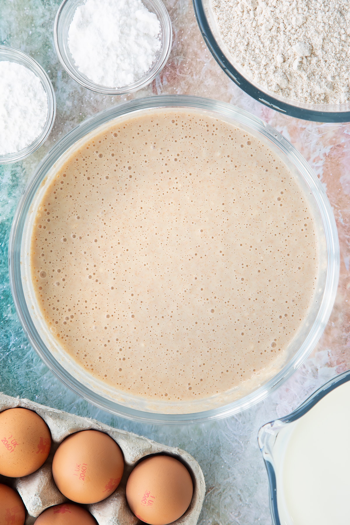 Overhead shot of flour milk and eggs mixed in a large clear bowl