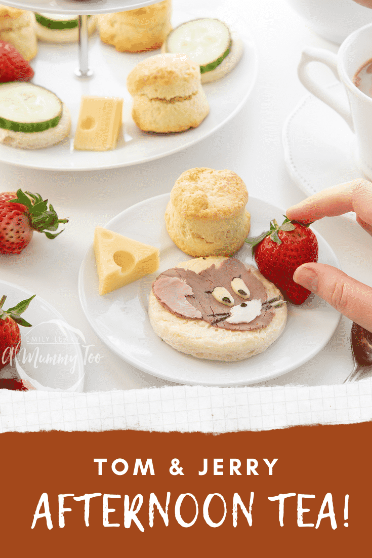 Hand reaching in to grab a strawberry from the Tom and Jerry afternoon tea plate. Some text at the bottom describes the image for Pinterest.