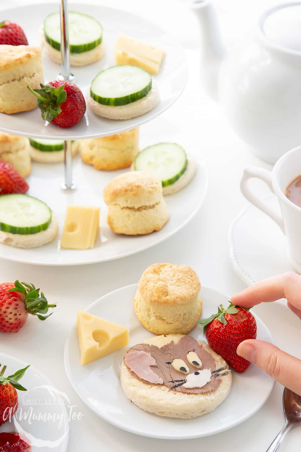 Hand reaching in to grab a strawberry from the plate of Tom and Jerry afternoon tea.