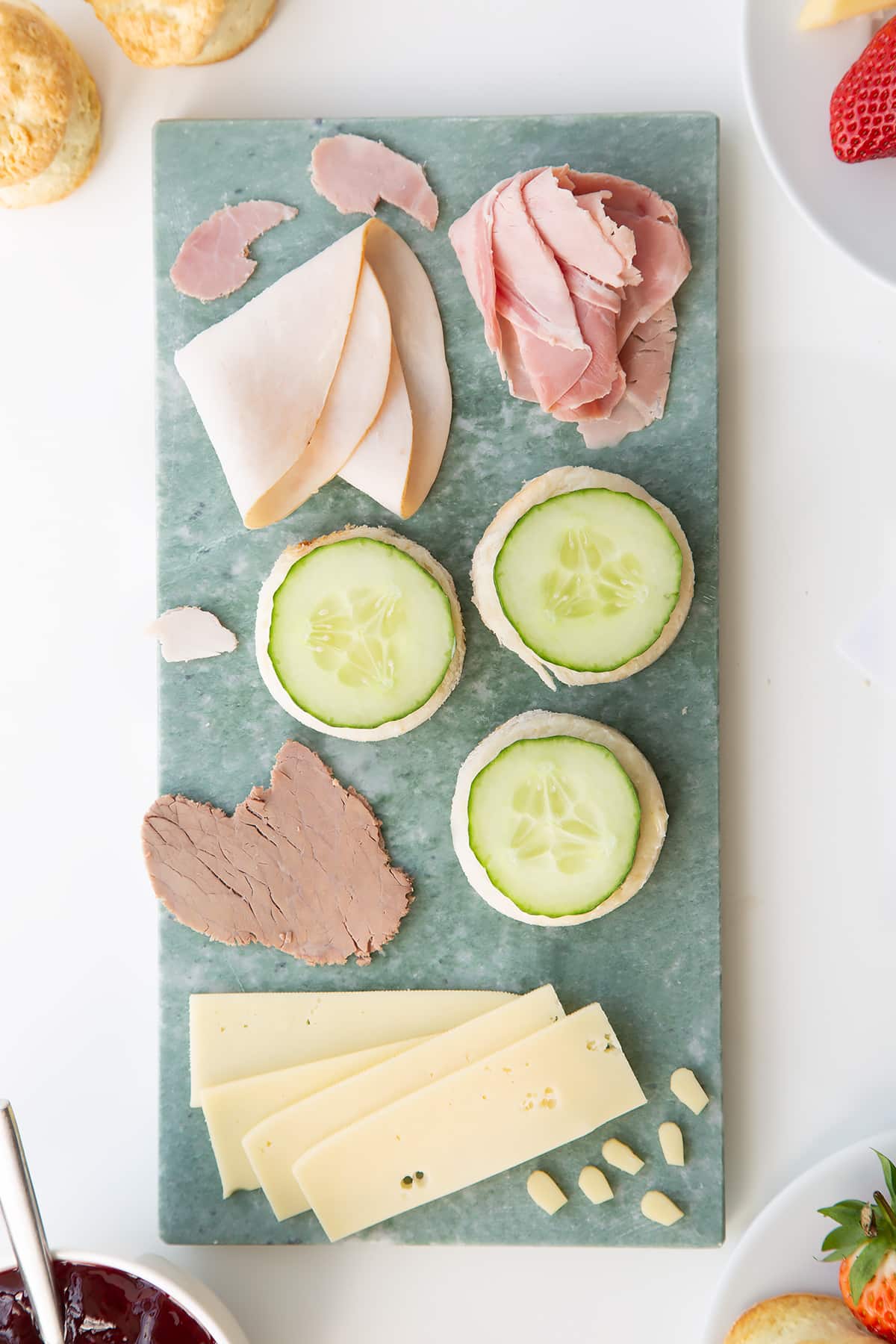 Overhead shot of the open cucumber sandwhiches being assembled on a green chopping board.