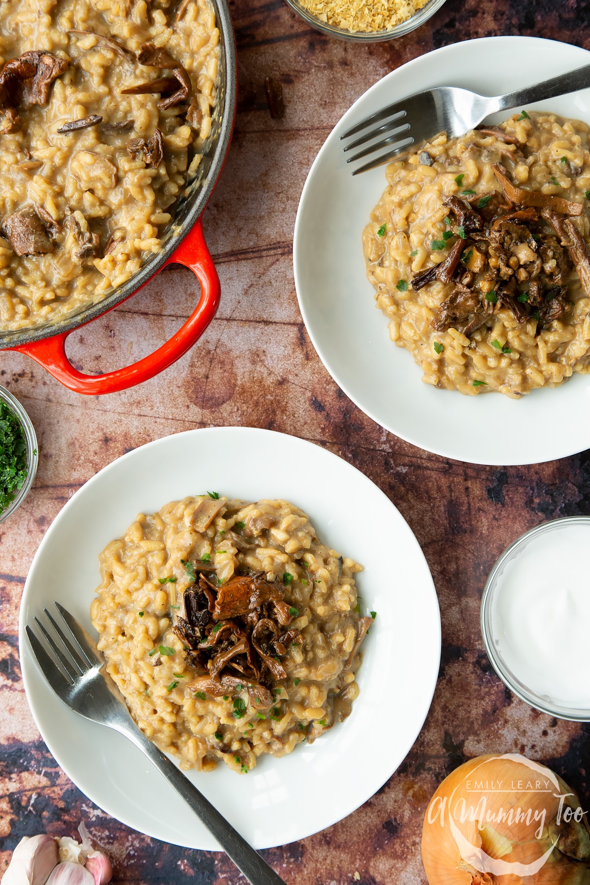 Vegan mushroom risotto in two shallow white bowls with forks, shown from above. The pot of risotto is also visible.