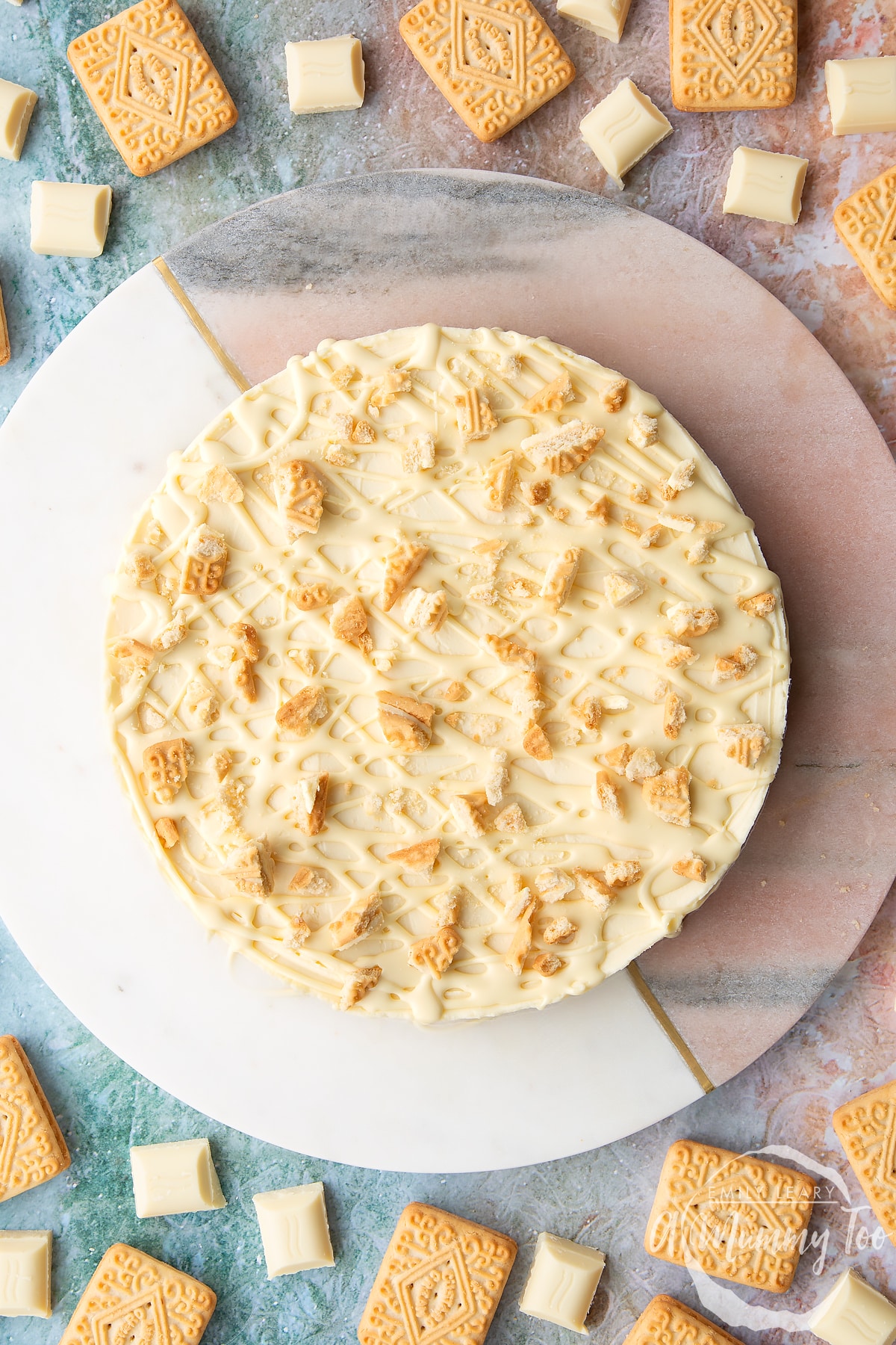 Overhead shot of white chocolate cheesecake topped with white chocolate drizzle and custard cream biscuit crumbs