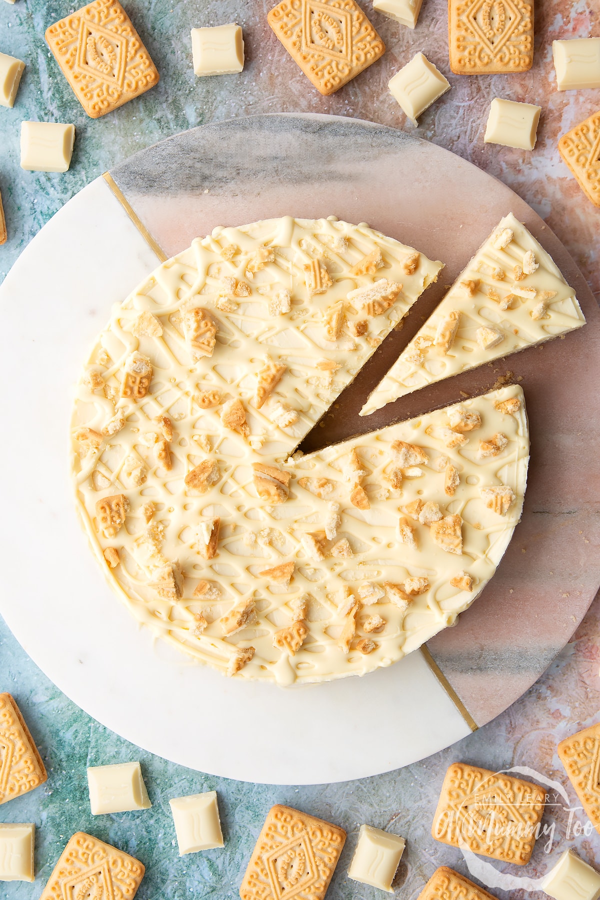 Overhead shot of white chocolate cheesecake topped with white chocolate drizzle and custard cream biscuit crumbs with a slice cut out