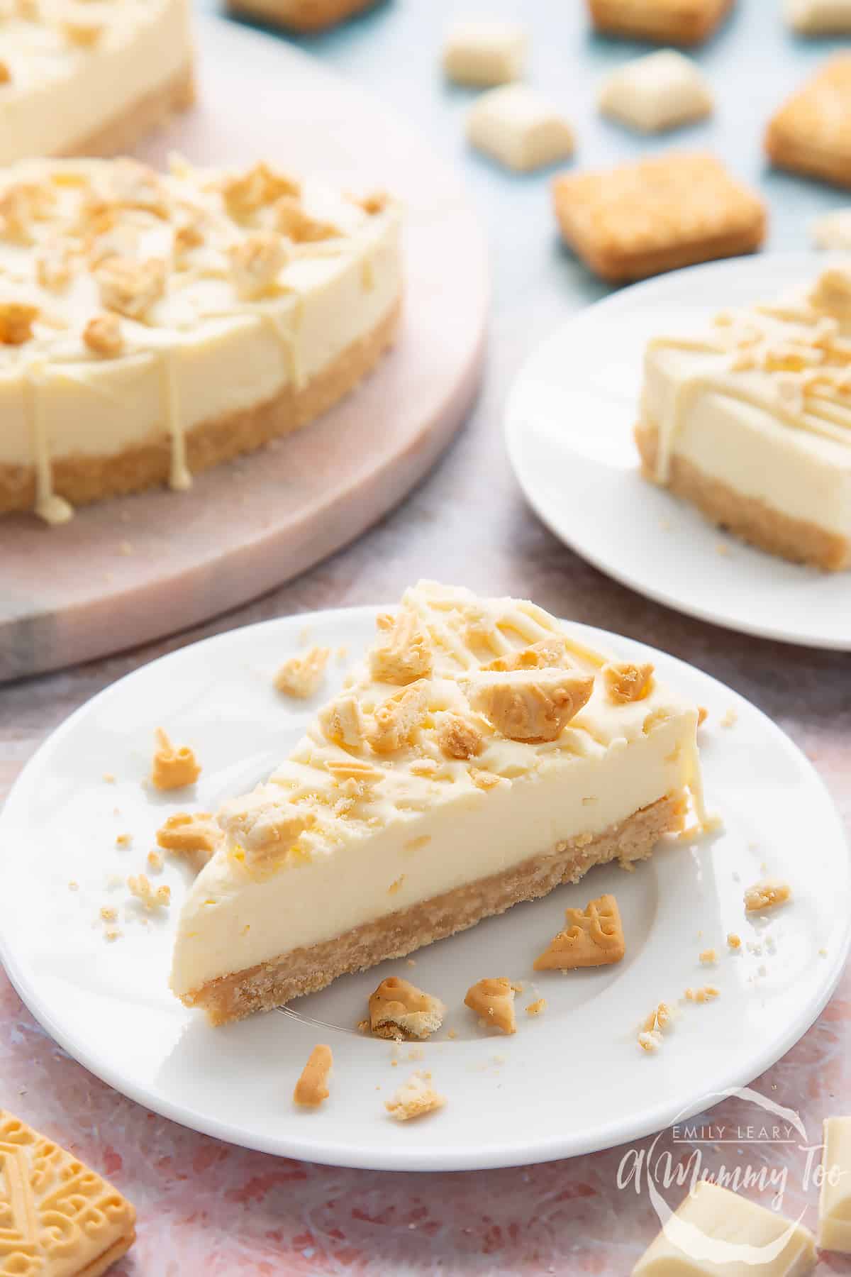 Front view shot of a piece of white chocolate cheesecake toppedw ith custard cream biscuit crumbs on a white plate