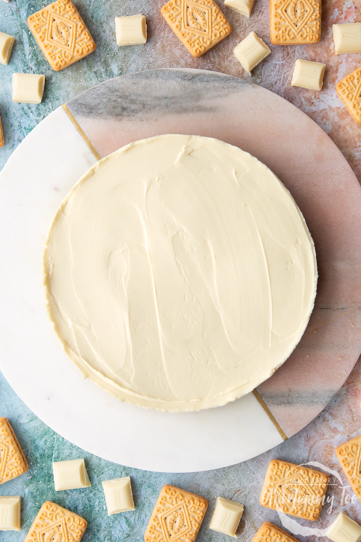 Overhead shot of white chocolate cheesecake on a marble board with the A Mummy Too logo in the corner