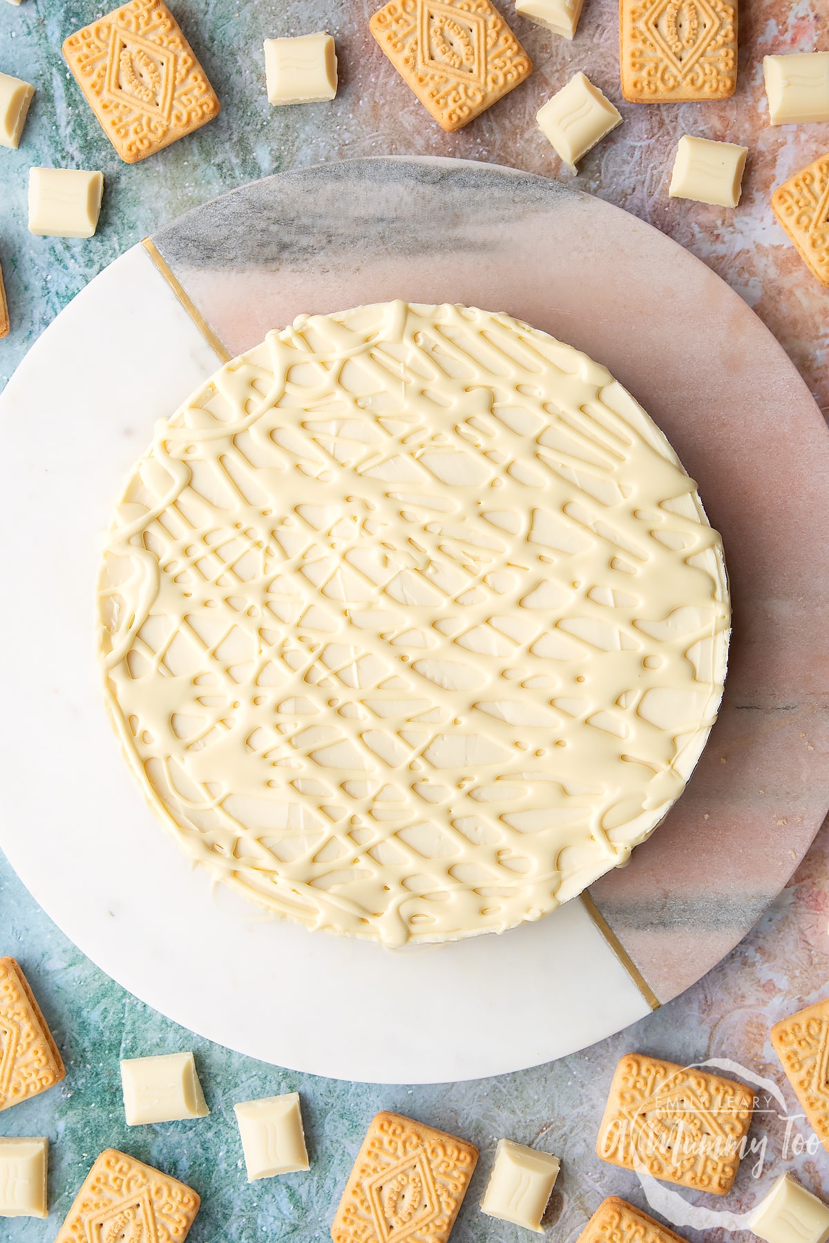 Overhead shot of white chocolate cheesecake with melted white chocolate drizzled on top with the A Mummy Too logo in the corner