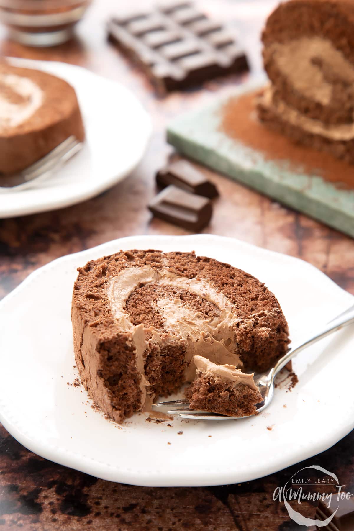 A slice of Chocolate Swiss roll on a white plate. Some of it has been eaten. A fork rests with some sponge on it.