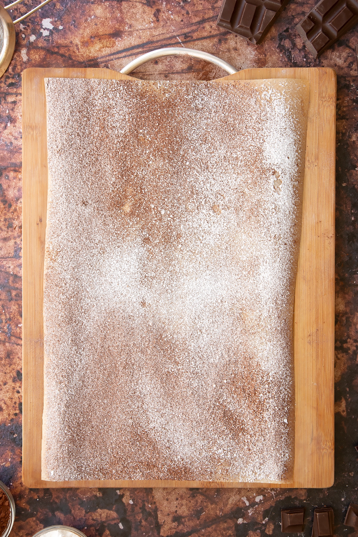 Wooden board topped with a piece of baking paper, dusted with cocoa and icing sugar.