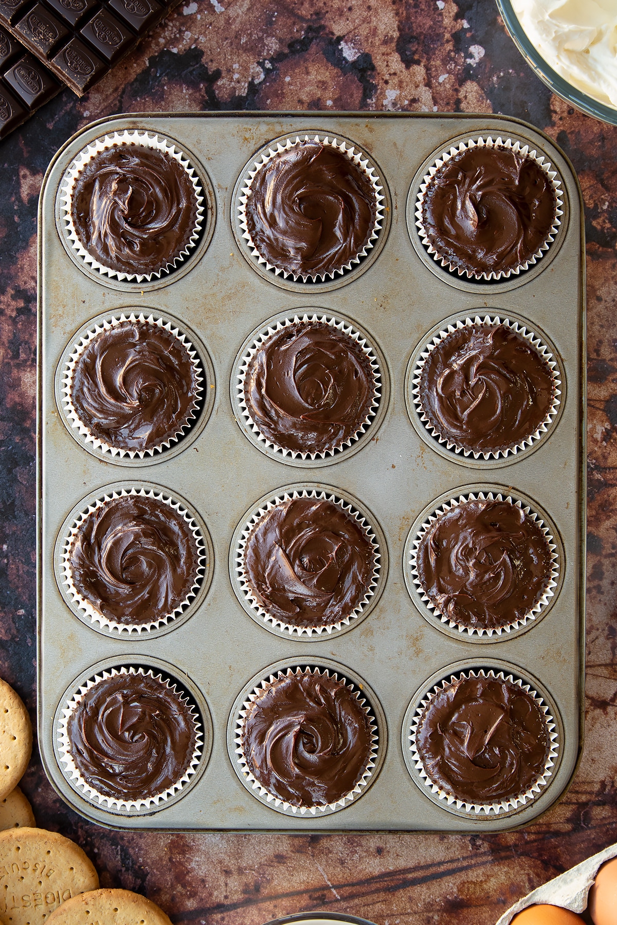 Chocolate cheesecake cupcakes freshly topped with ganache in a muffin tray.
