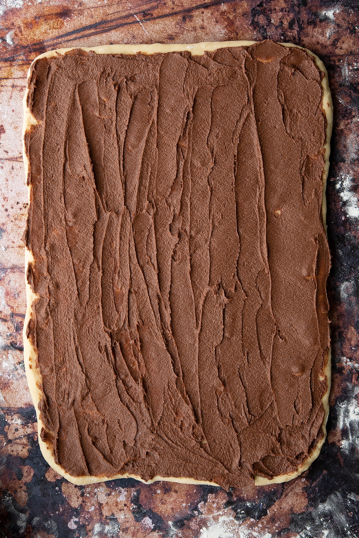 Overhead shot of dough rolled out to a rectangle with chocolate cinnamon spread on top