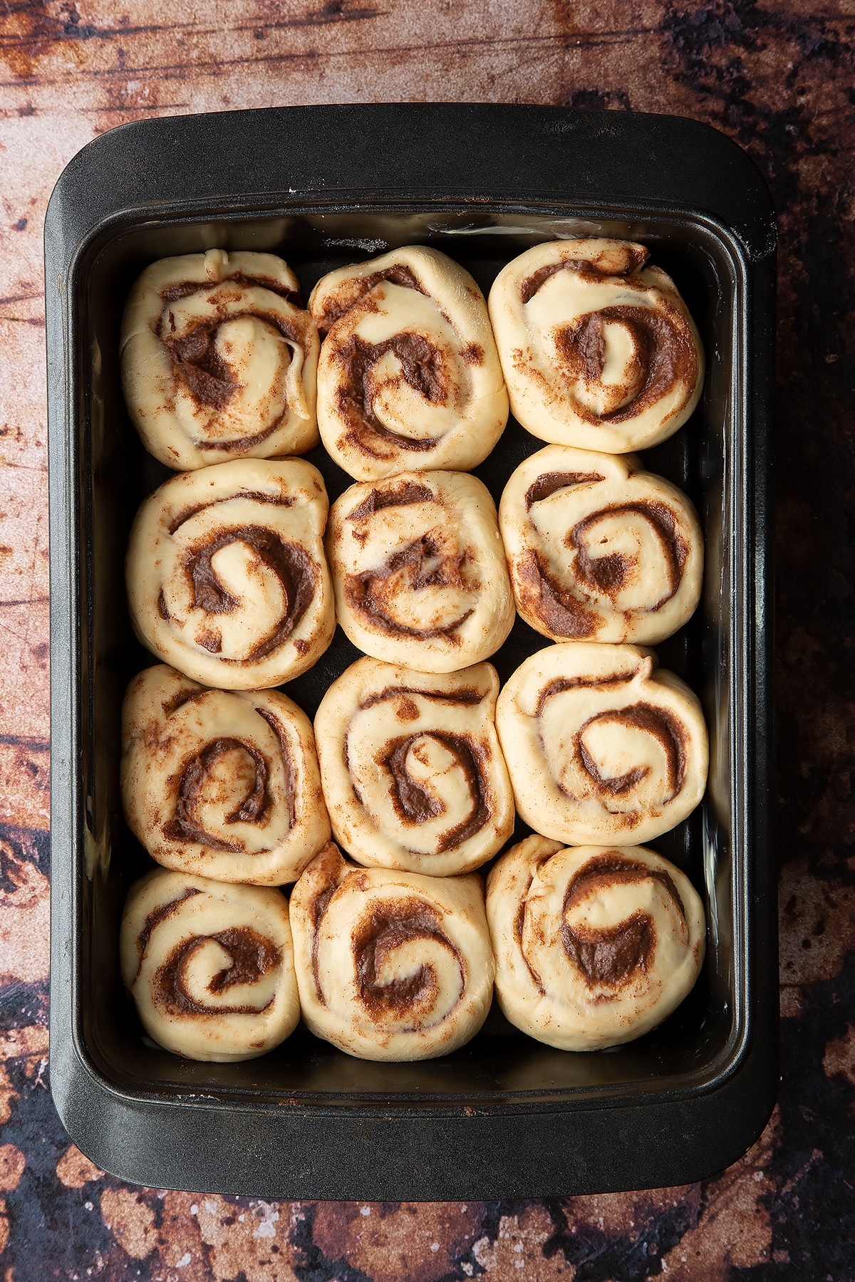 Overhead shot of Chocolate cinnamon bun dough rolled up into sections laid out in a deep baking tray