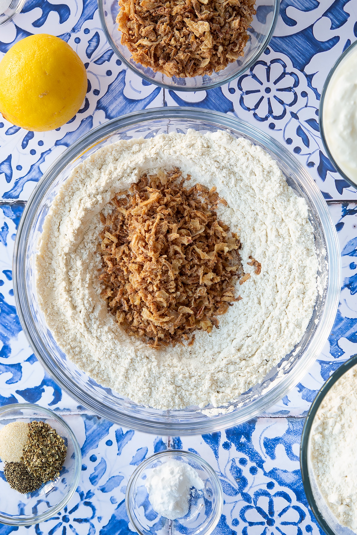 Flour and seasoning stirred together in a mixing bowl with crispy fried onions. Ingredients to make onion soda bread surround the bowl.