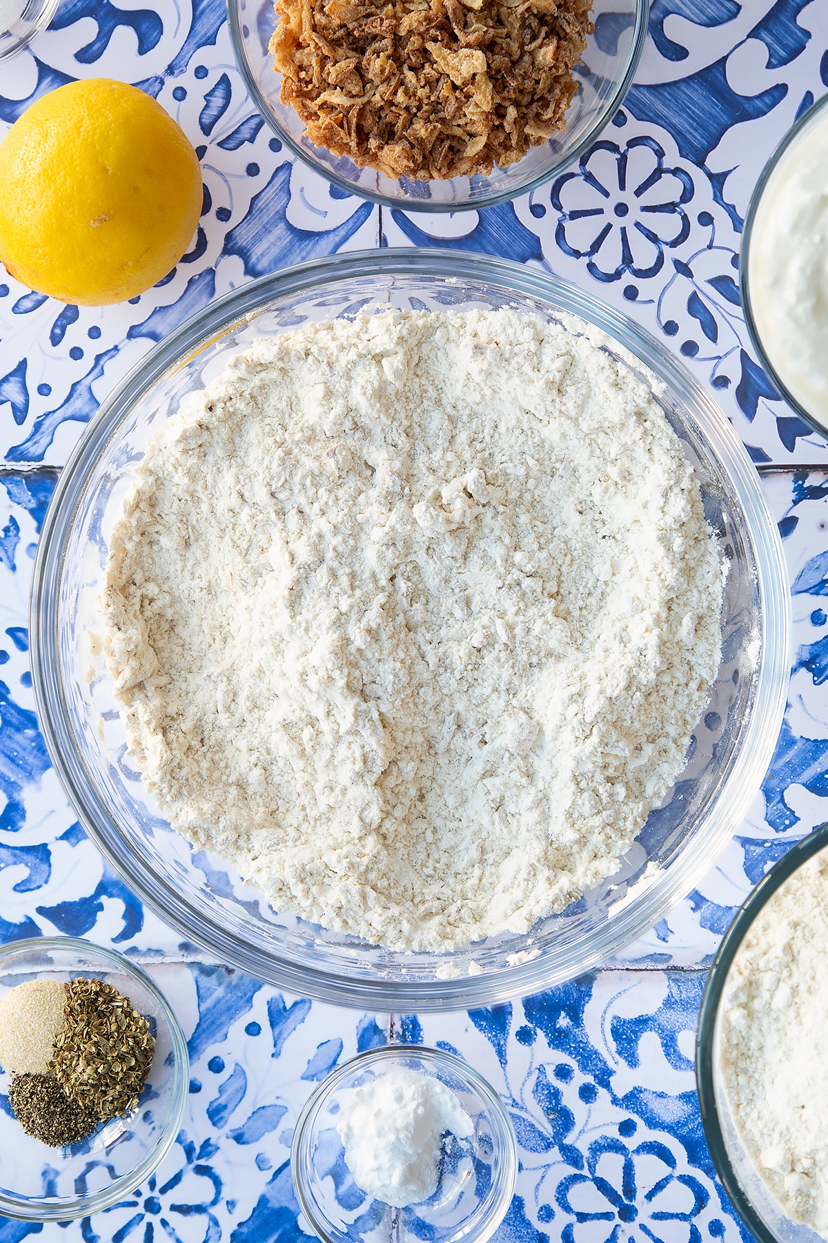 Flour, seasoning and crispy fried onions stirred together in a mixing bowl. Ingredients to make onion soda bread surround the bowl.