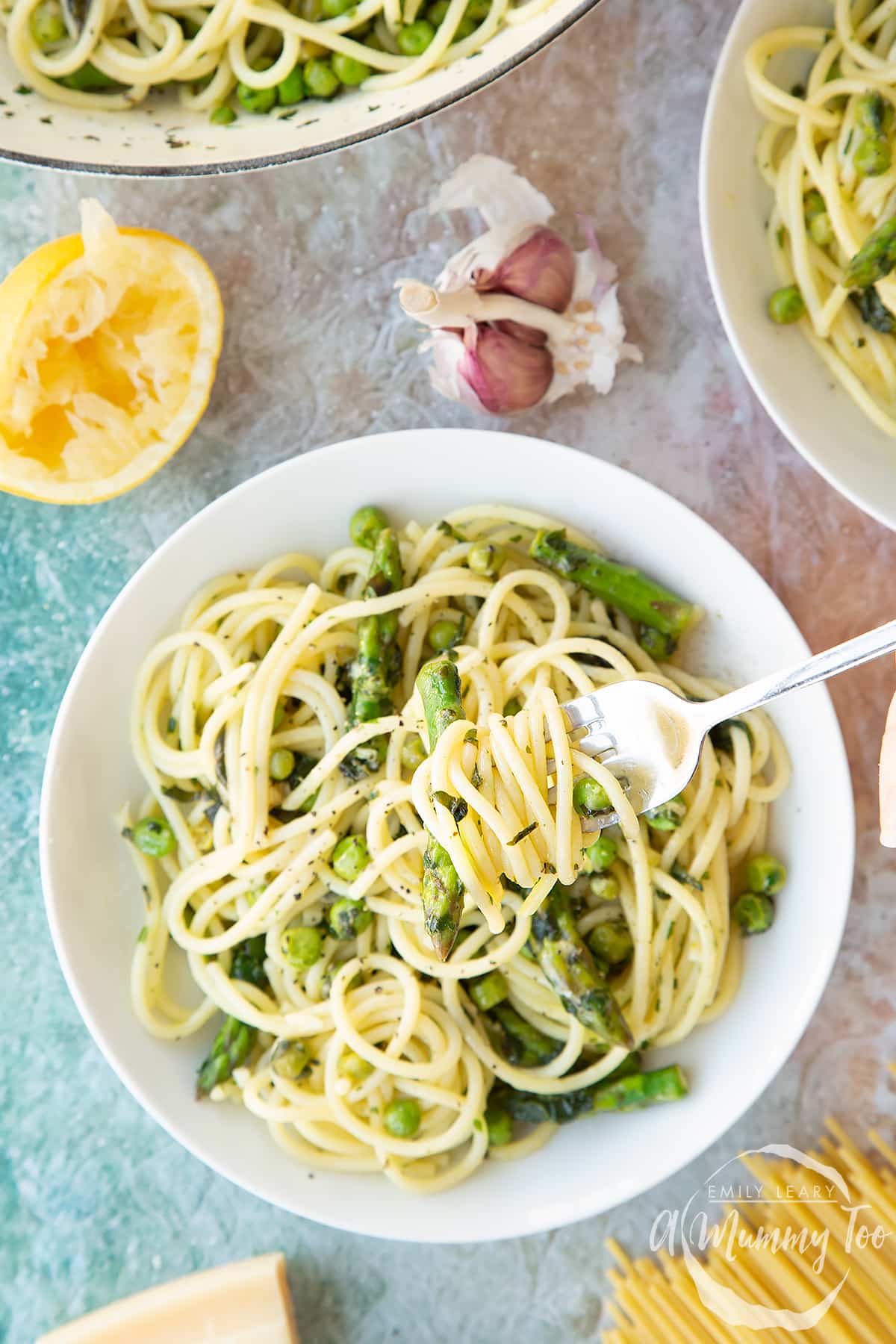 Summer spaghetti with spinach, basil, asparagus and peas, served in a white bowl. Shown from above, a hand holds a fork with spaghetti twisted on it.