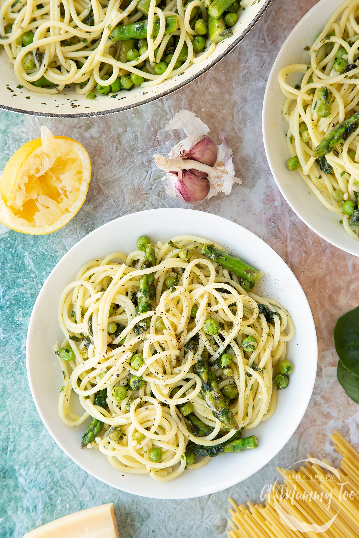 Summer spaghetti with spinach, basil, asparagus and peas, served in white bowls. Shown from above.