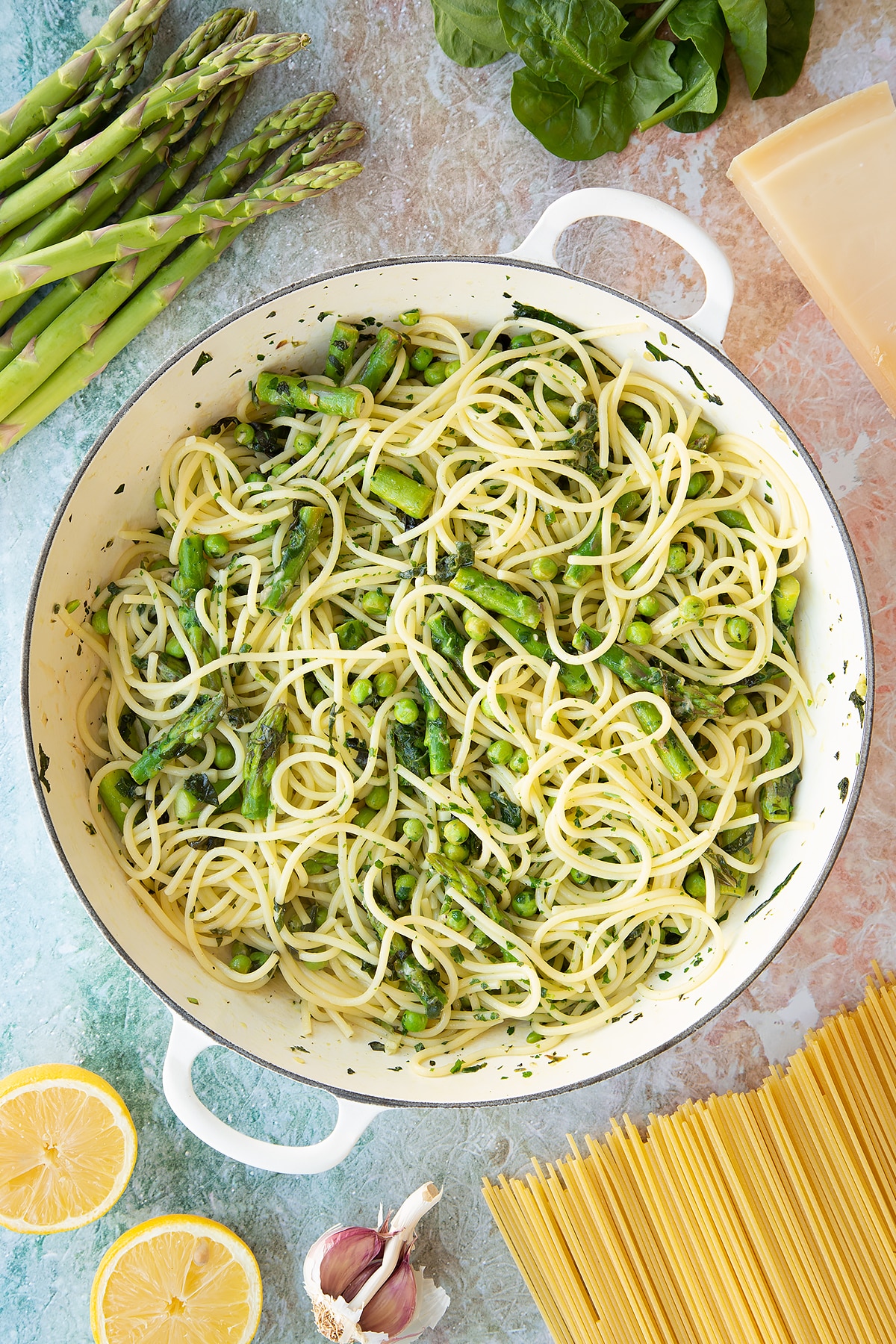 Summer spaghetti with spinach, basil, asparagus and peas in a large, shallow saucepan.