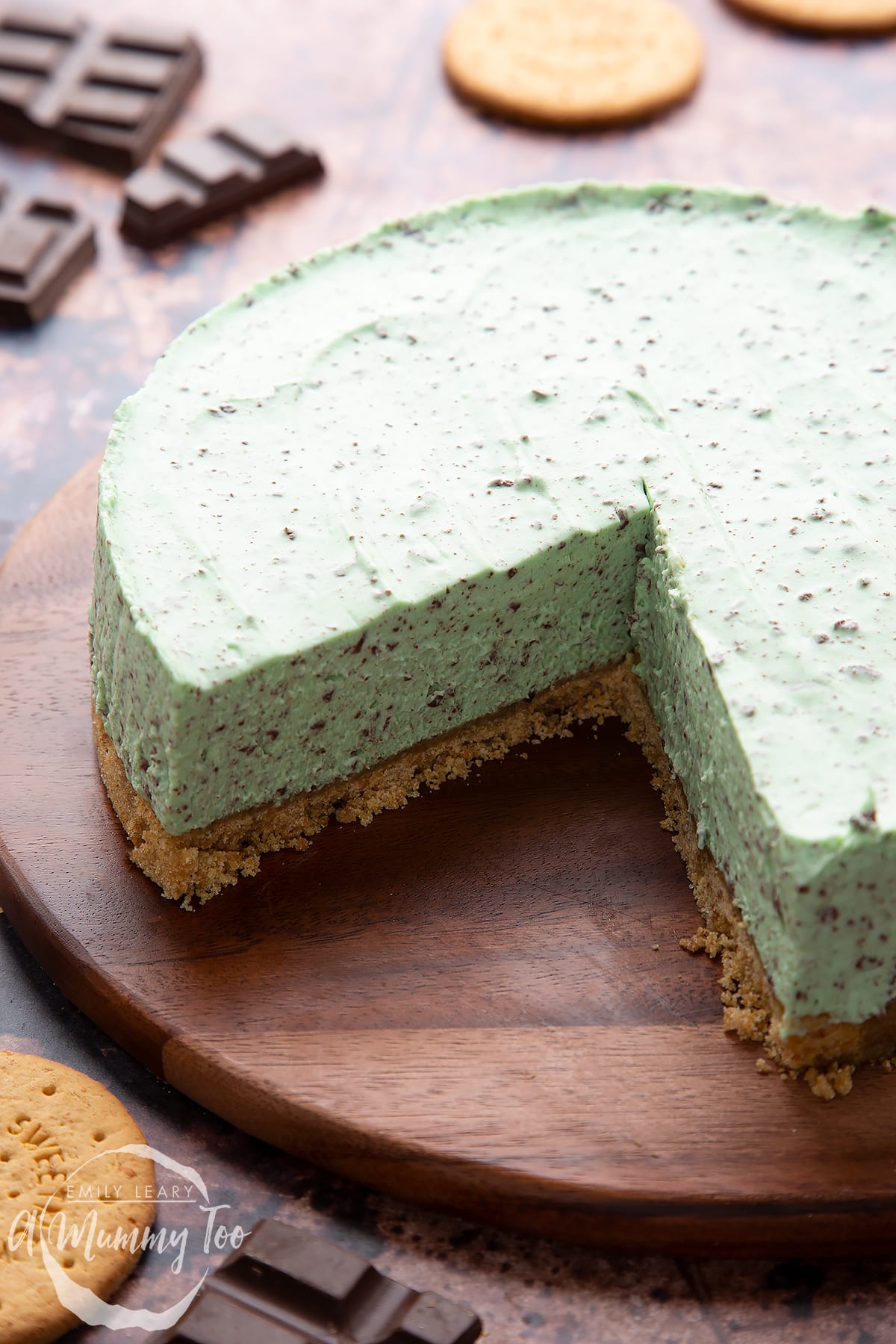 A no bake mint cheesecake with a biscuit base on a wooden board with a large slice removed.