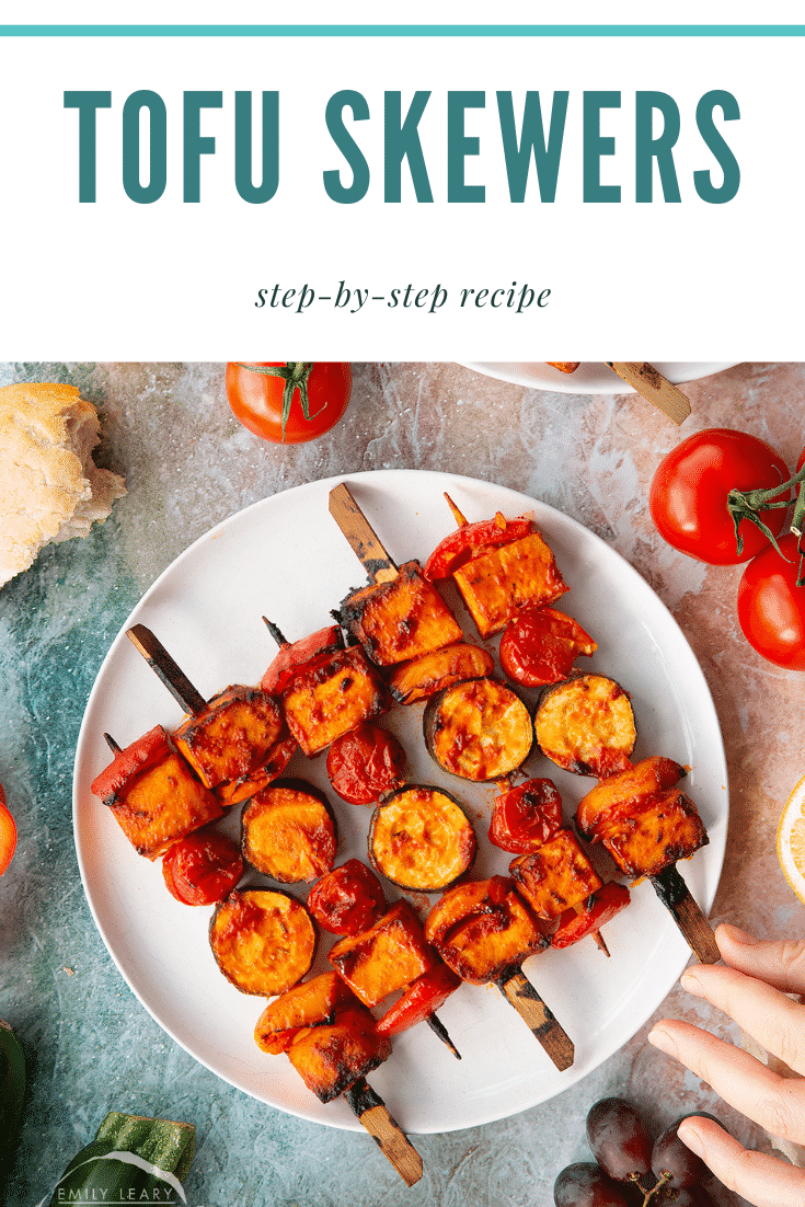 Tofu skewers arranged on a white plate. A hand reaches for one. Caption reads: Tofu skewers. Step-by-step recipe.