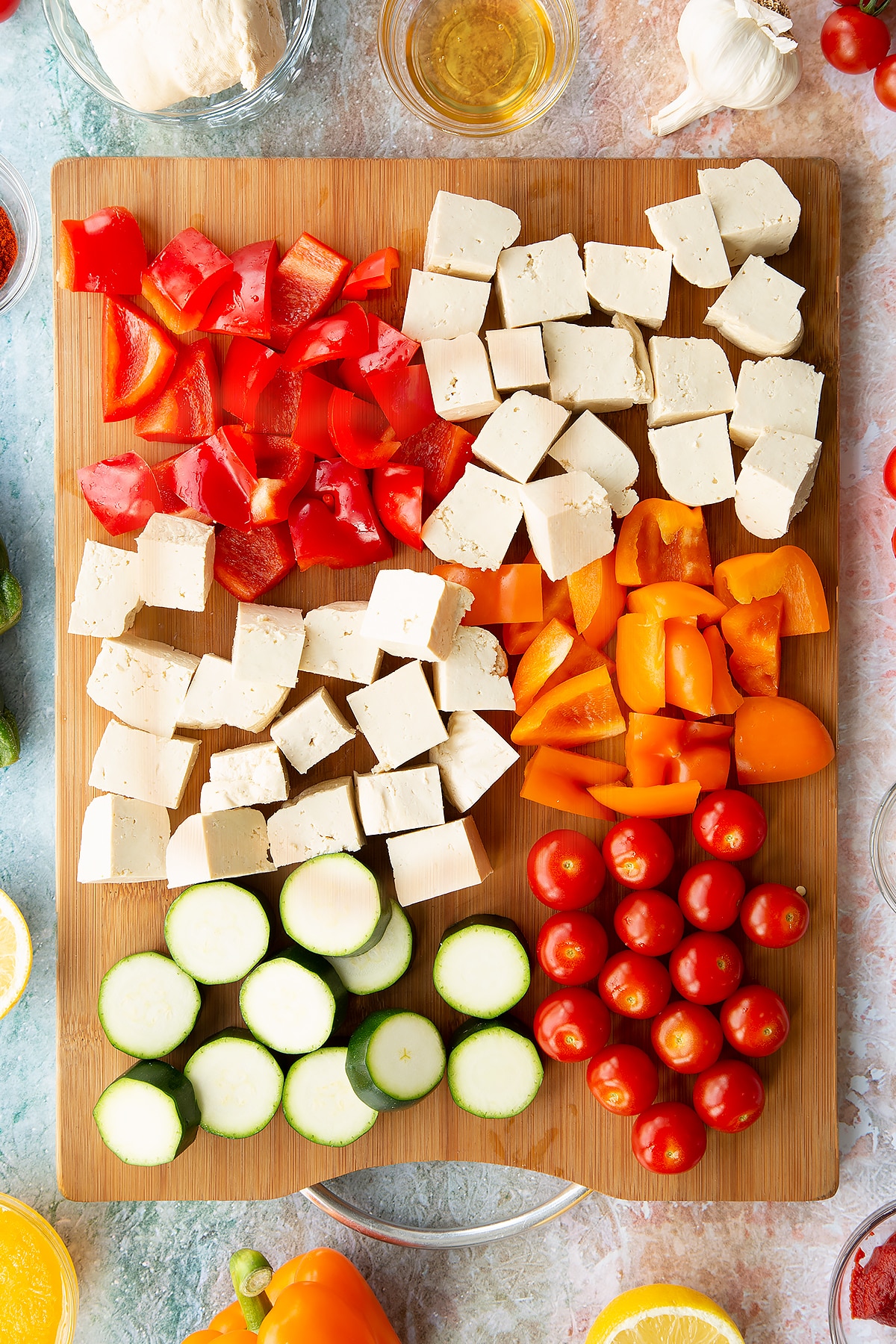 All the ingredients for the tofu skewers on a board: whole cherry tomatoes, thickly sliced courgette, chopped red and orange peppers, cubed tofu.