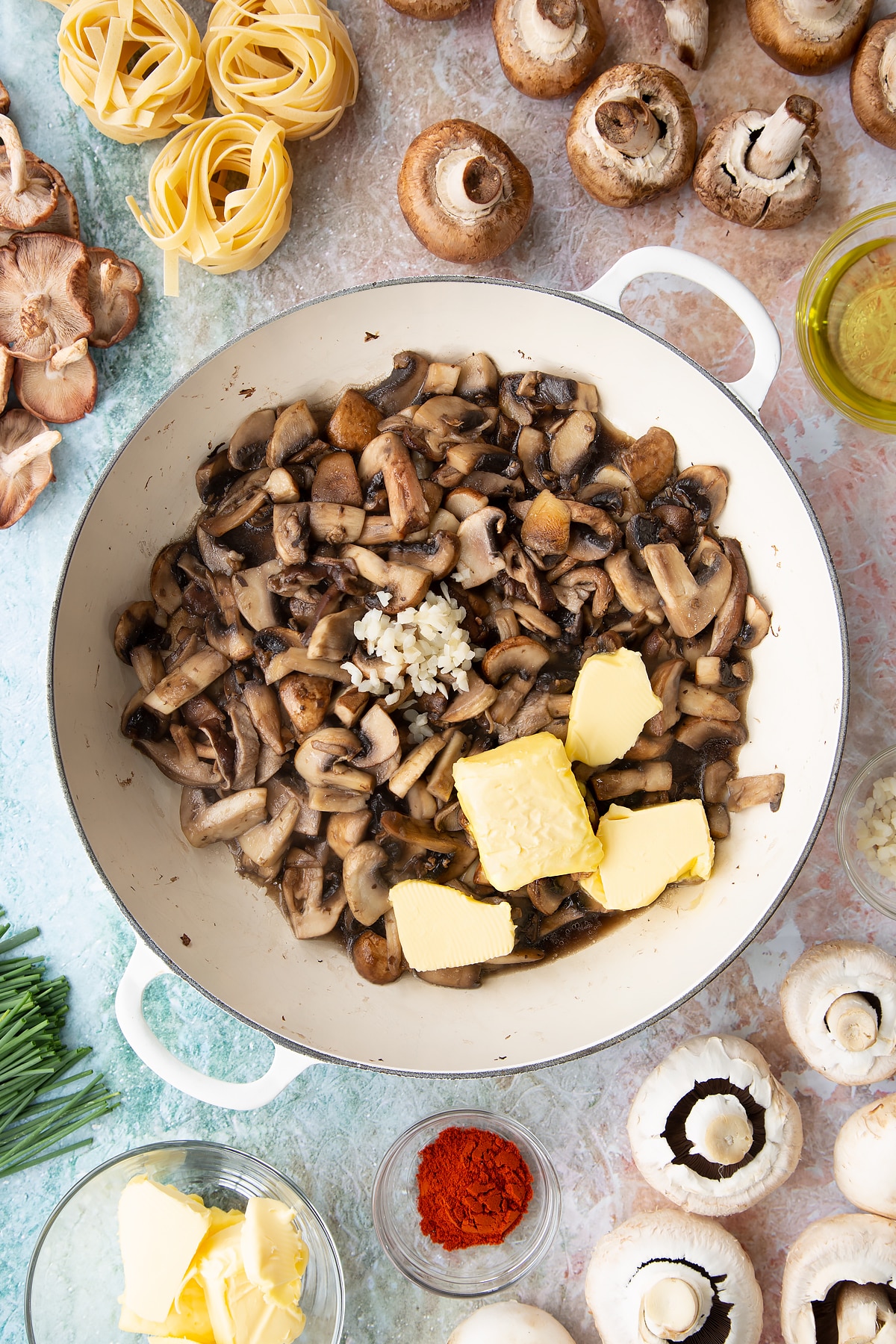 a large white pan with cooked mushrooms, butter and garlic in the bottom, with ingredients surrounding the pan.