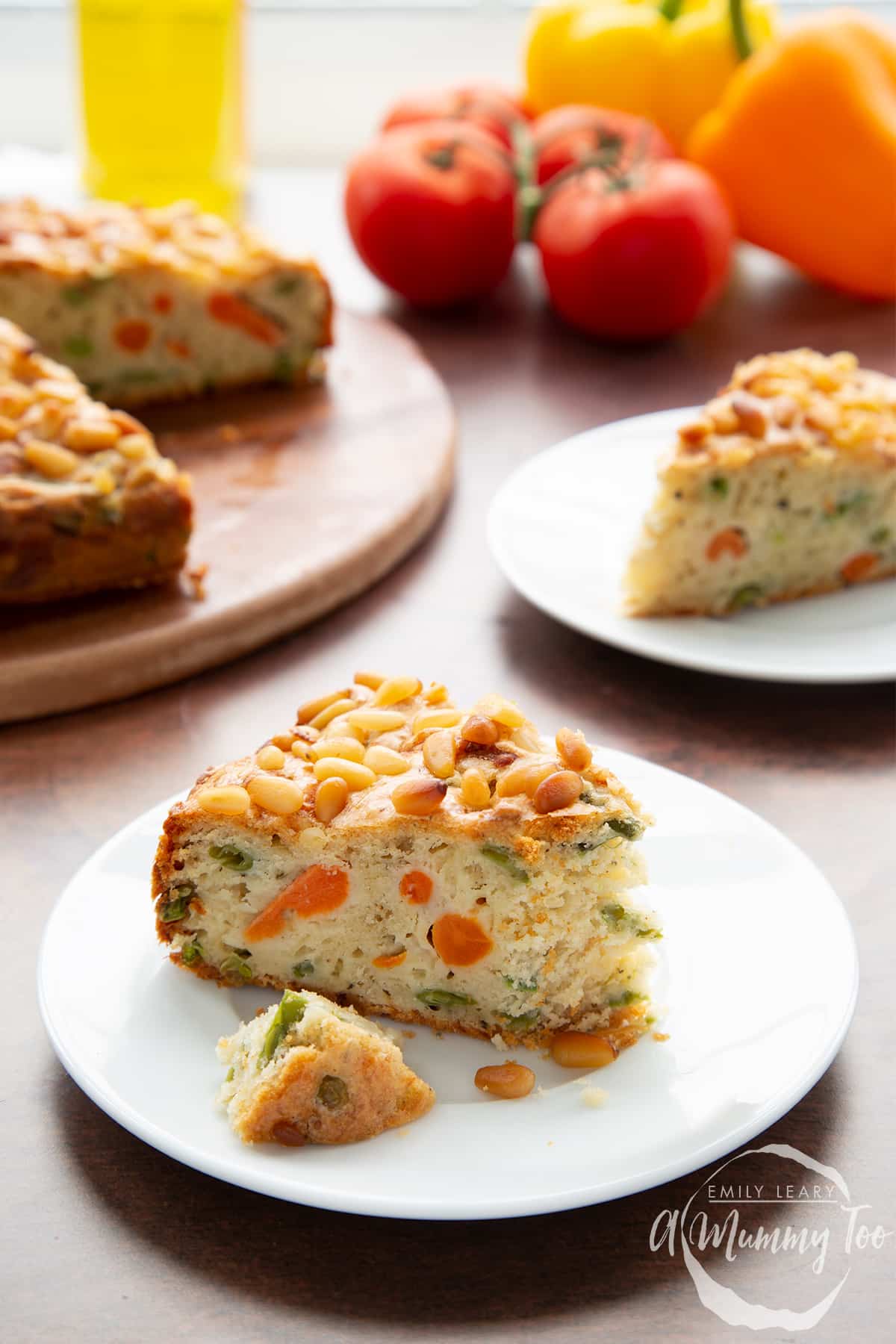 A slice of vegetable cake on a white plate. A piece has been broken off. There is more cake in the background.
