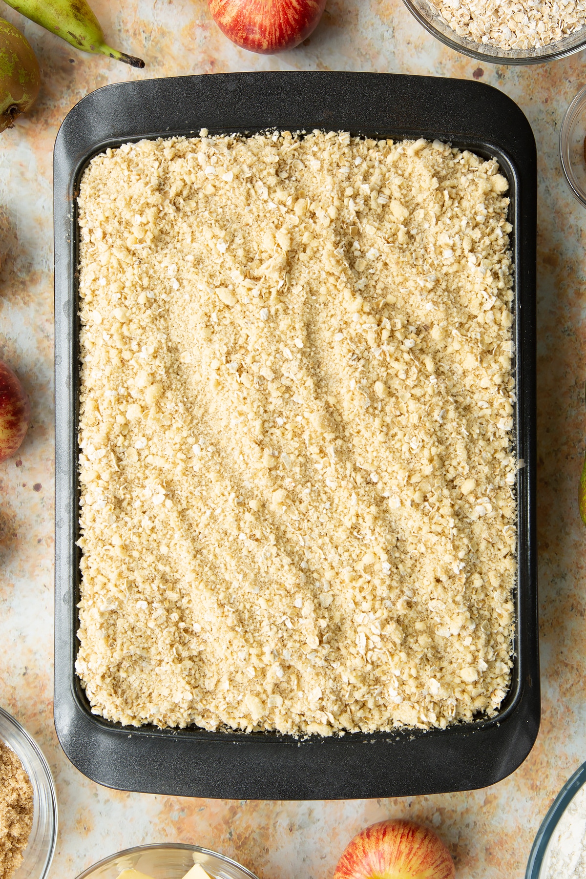 Oat crumble on top of apples and pears in a metal tray.