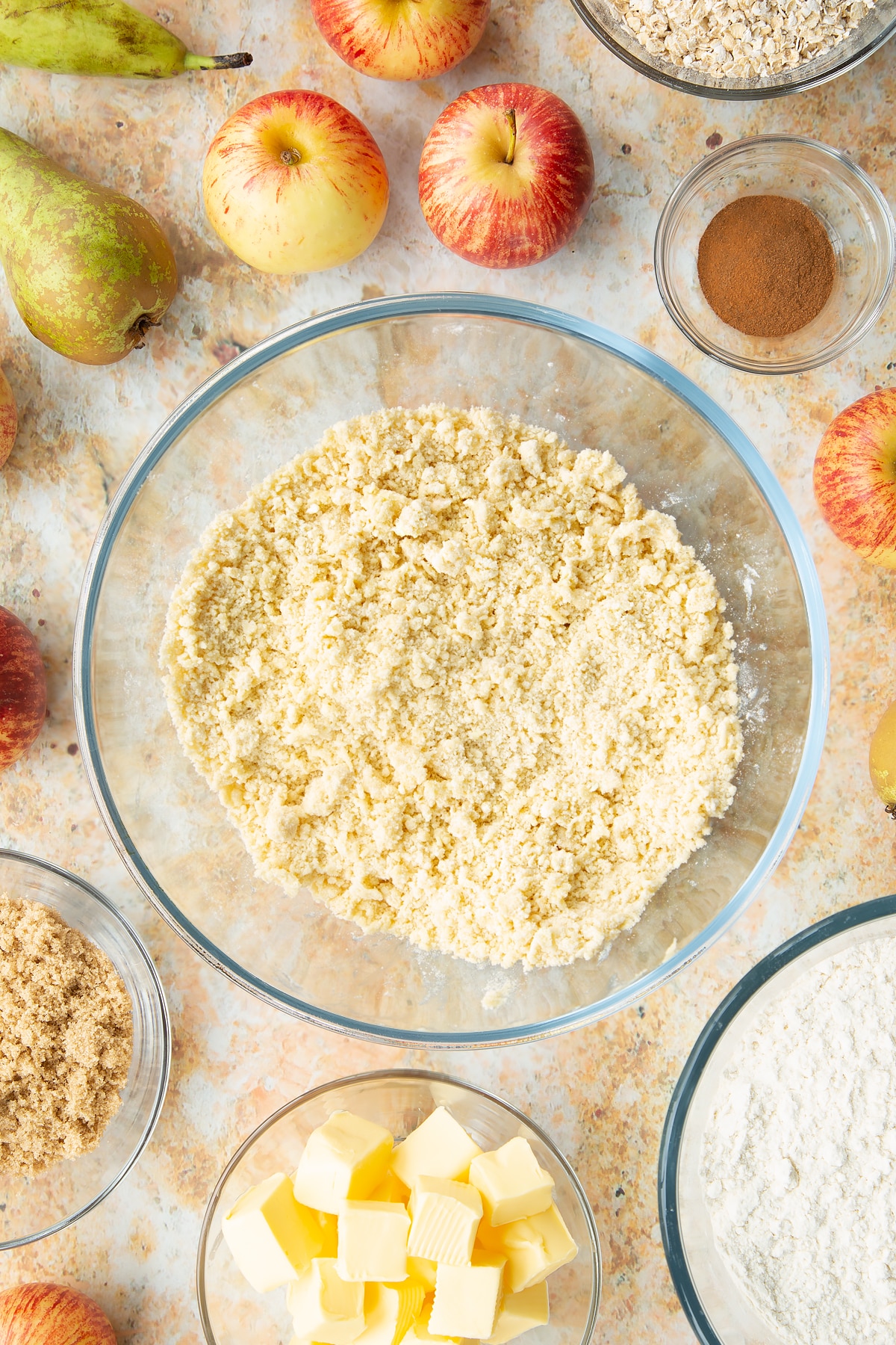 Flour and butter rubbed together in a mixing bowl. Ingredients to make easy apple pear crumble surround the bowl.