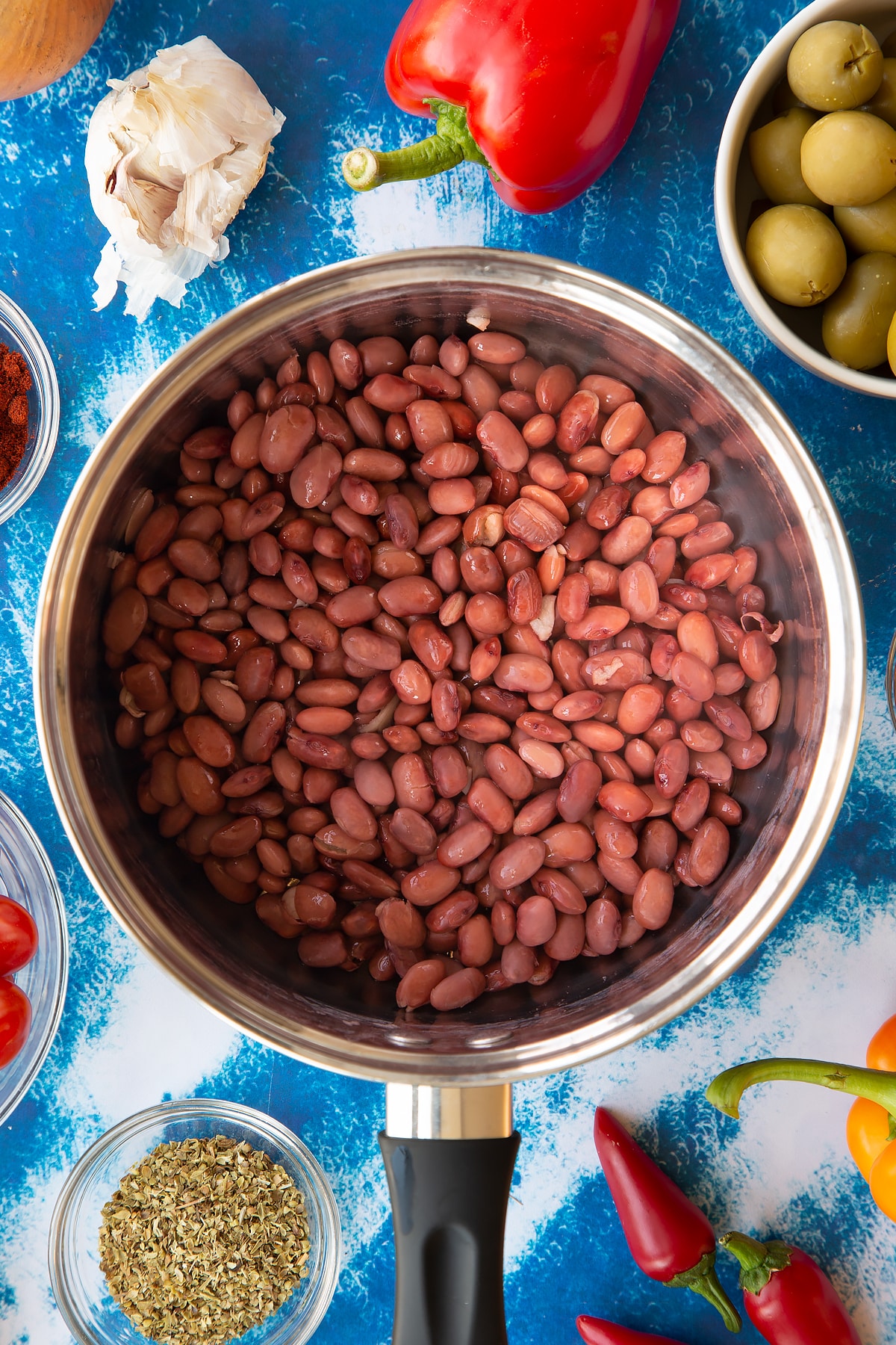 Cooked kidney beans in a saucepan. Ingredients to make easy Spanish rice and beans surround the pan.