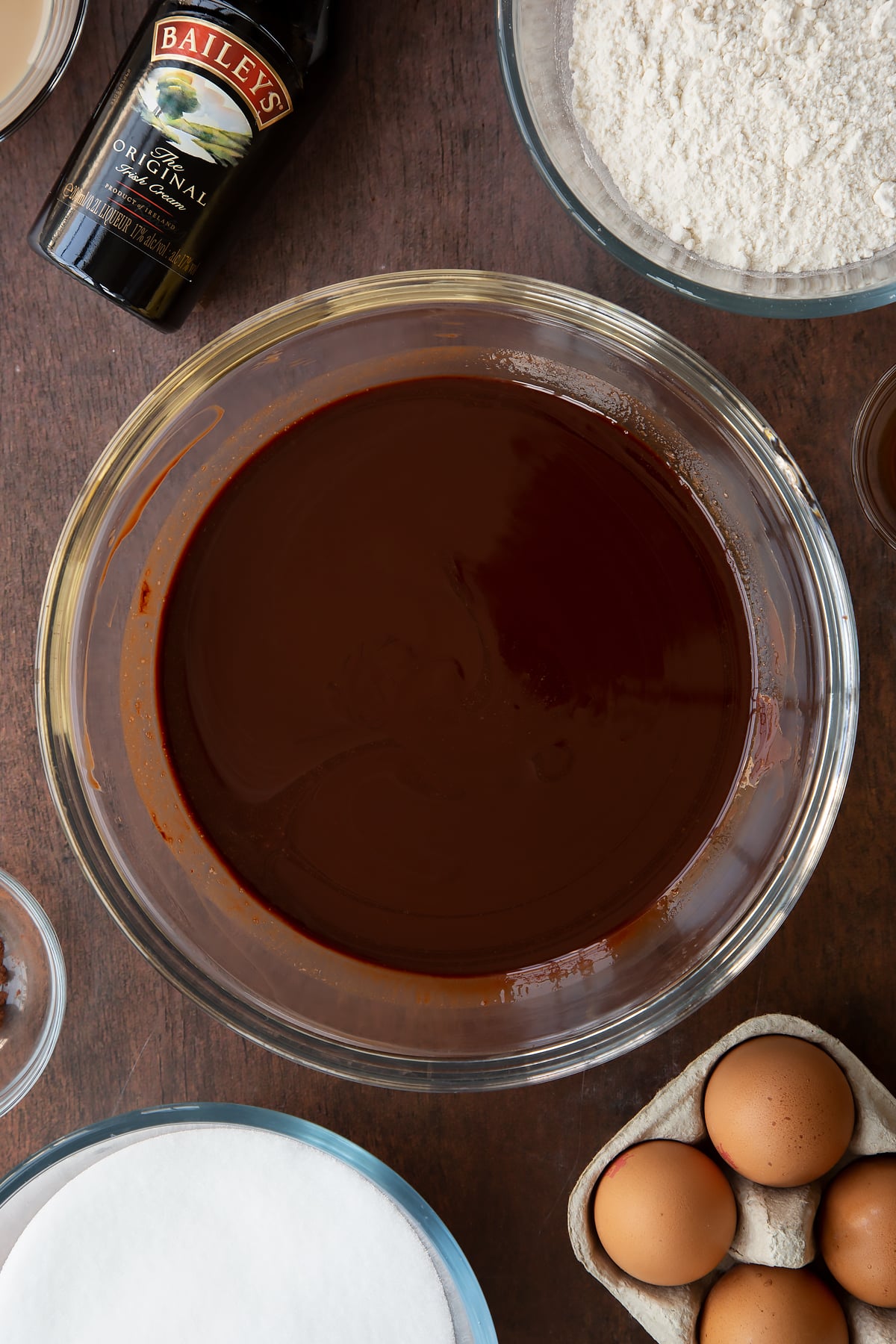 Melted chocolate and butter in a glass bowl. Ingredients to make Baileys brownies surround the bowl.