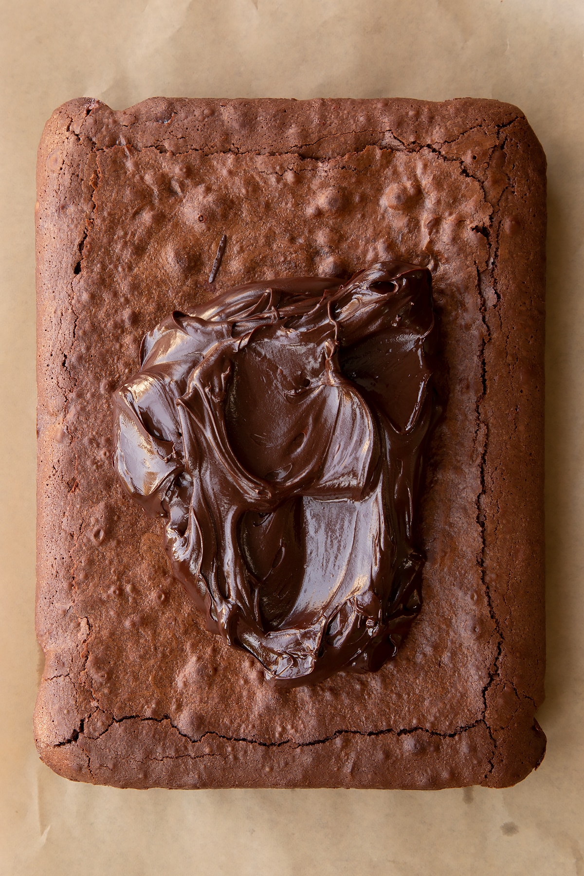 Baked candy cane brownie on baking paper with dark chocolate ganache on top.
