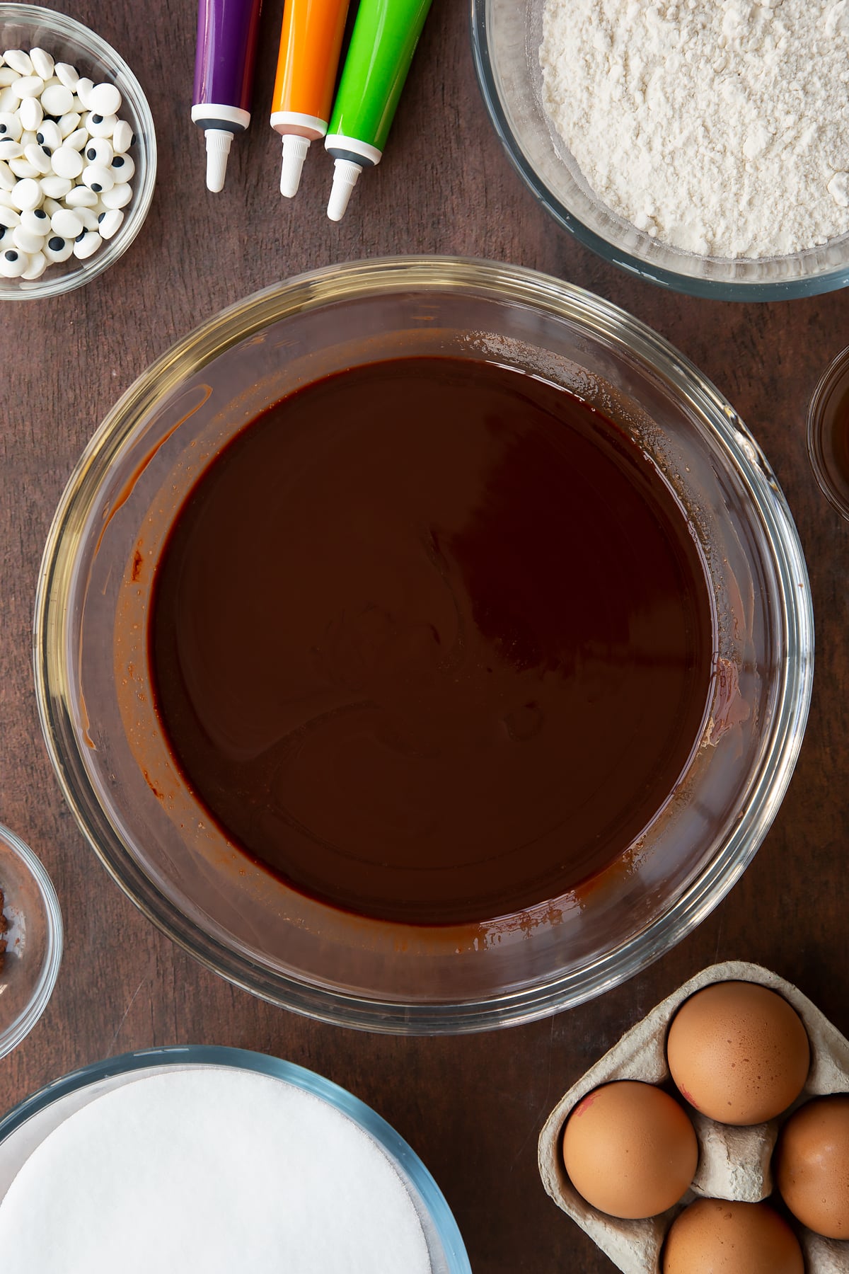 Melted butter and dark chocolate in a glass bowl. Ingredients to make Halloween brownies surround the bowl.