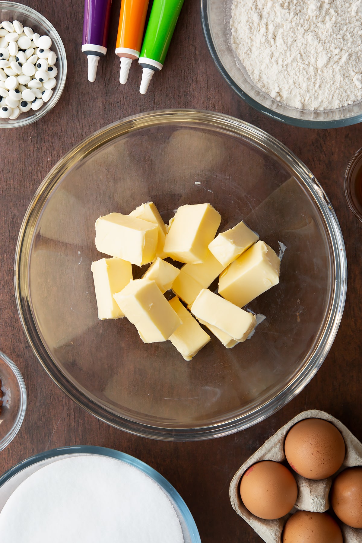 Cubed butter in a glass bowl. Ingredients to make Halloween brownies surround the bowl.