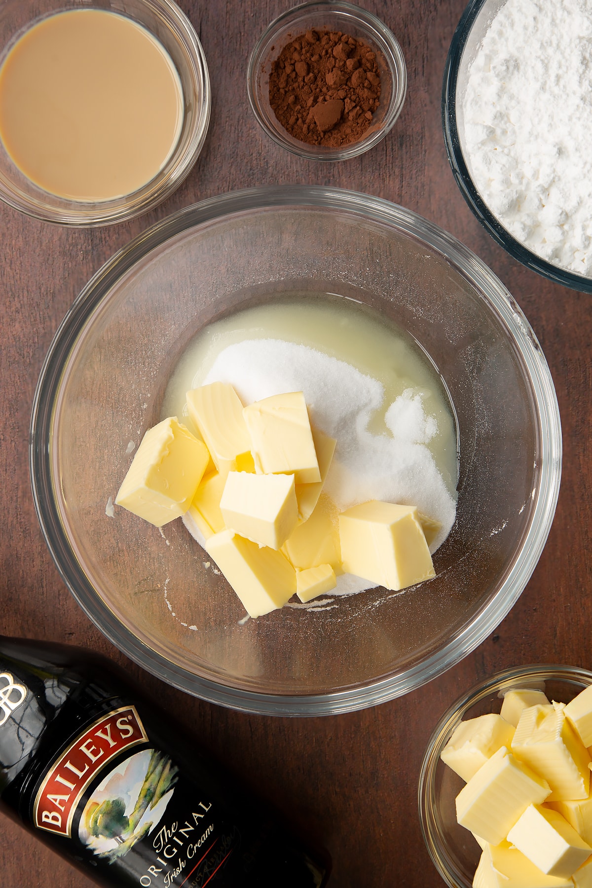 Butter, oil and sugar in a glass mixing bowl. Ingredients to make Baileys chocolate cupcakes surround the bowl.