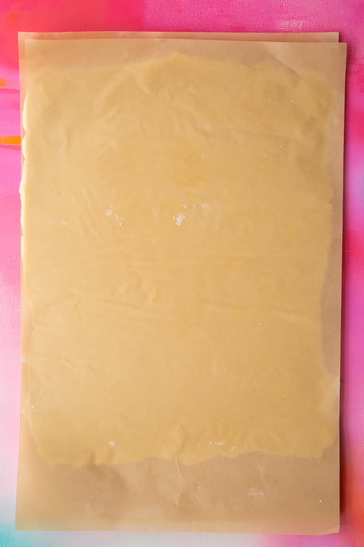 Gluten free pasty rolled out between two sheets of baking paper.