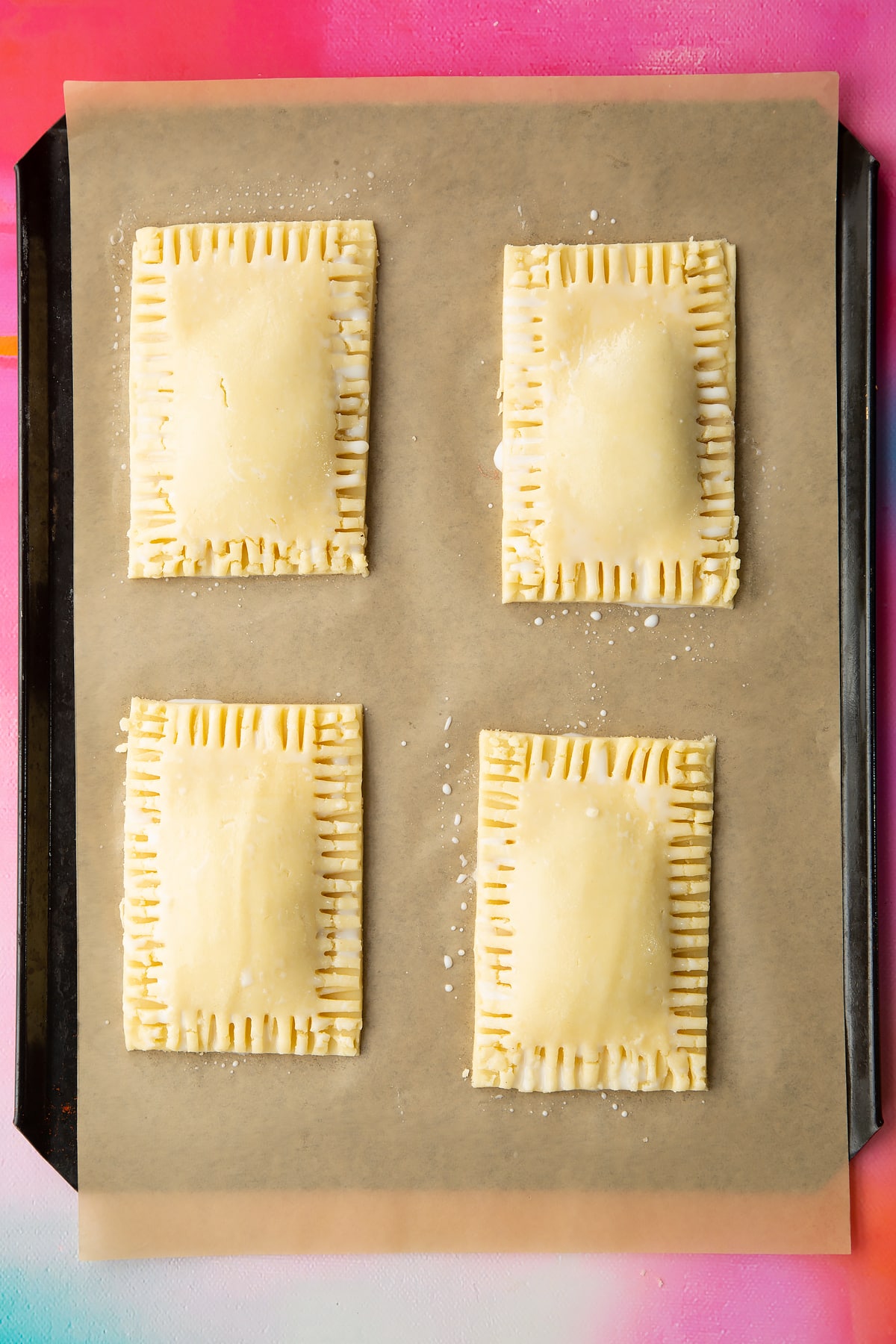 Four raw gluten free pop tarts, brushed with milk on baking tray lined with baking paper.