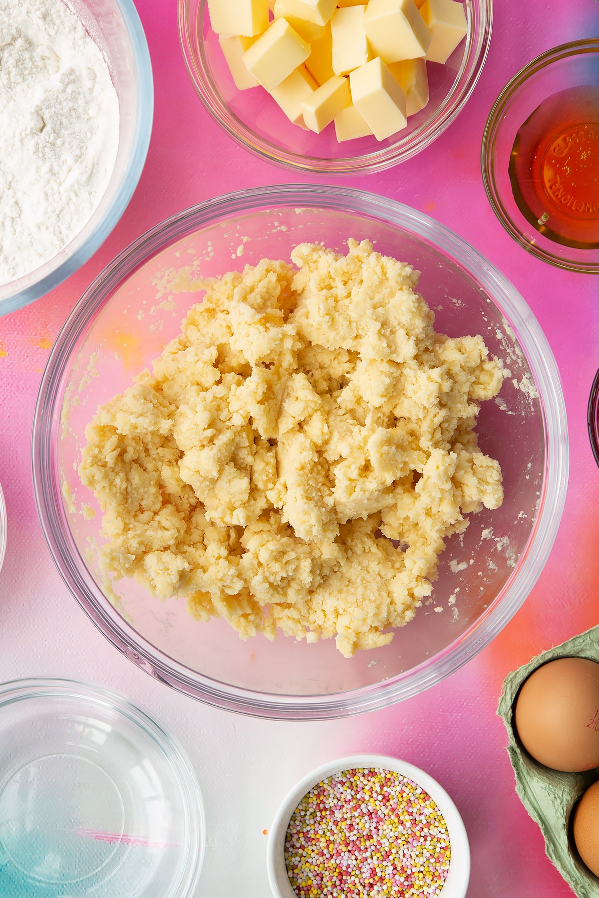 Butter, gluten free flour. sugar and eggs mixed together in a glass mixing bowl. Ingredients to make gluten free pop tarts surround the bowl.