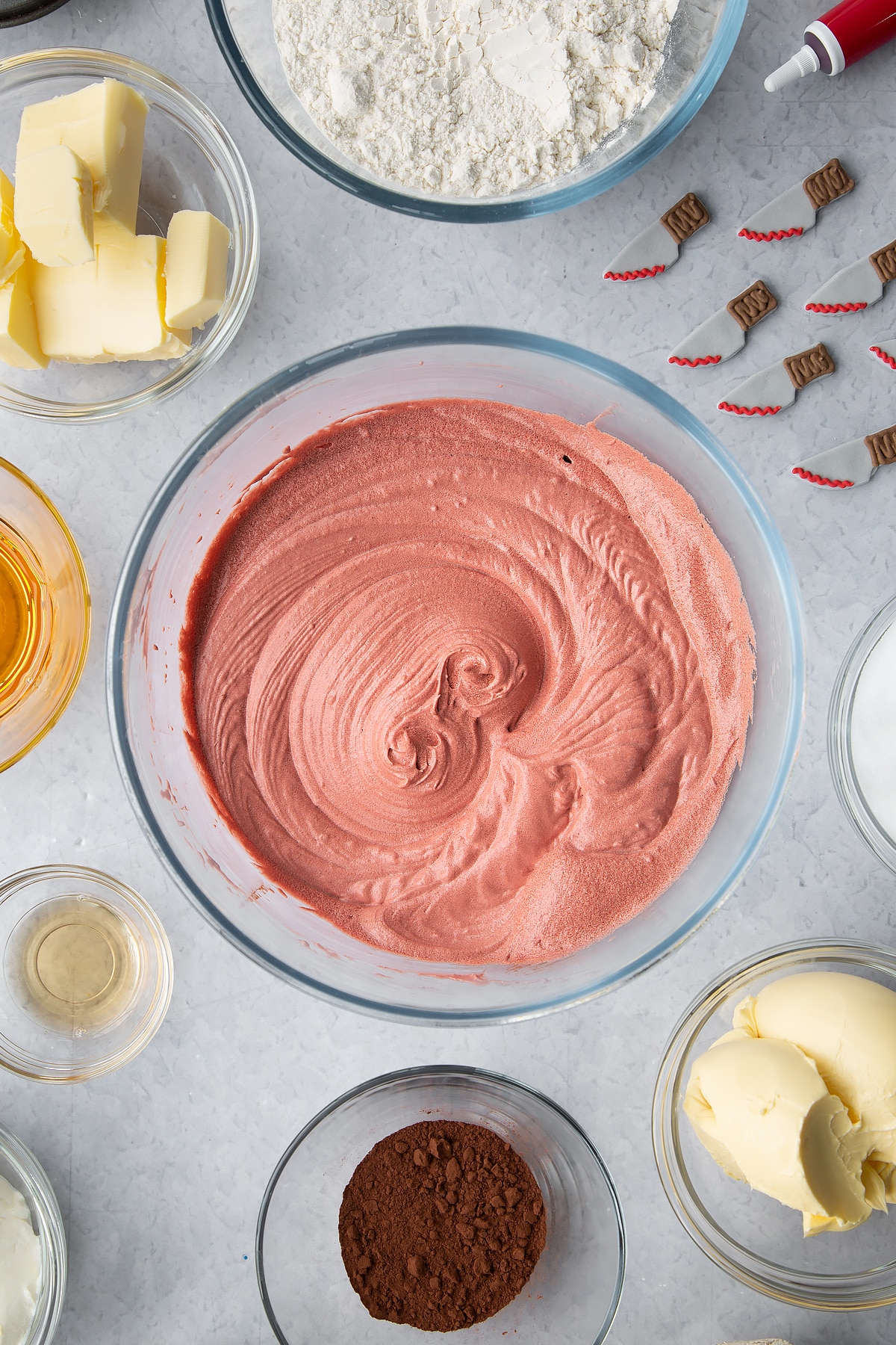 Red velvet cake batter in a glass bowl. Ingredients to make red velvet Halloween cupcakes surround the bowl.