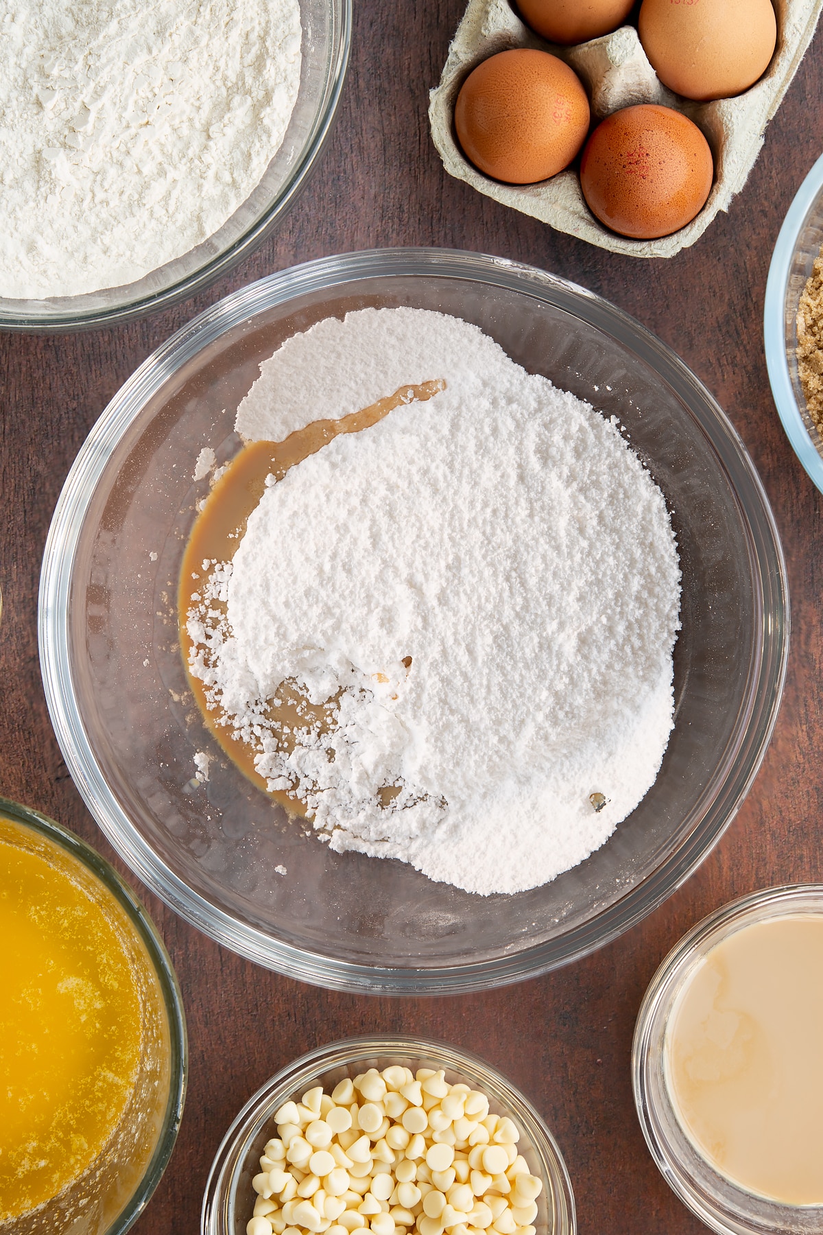 Icing sugar and Baileys in a glass mixing bowl. Ingredients to make Baileys blondies surround the bowl.