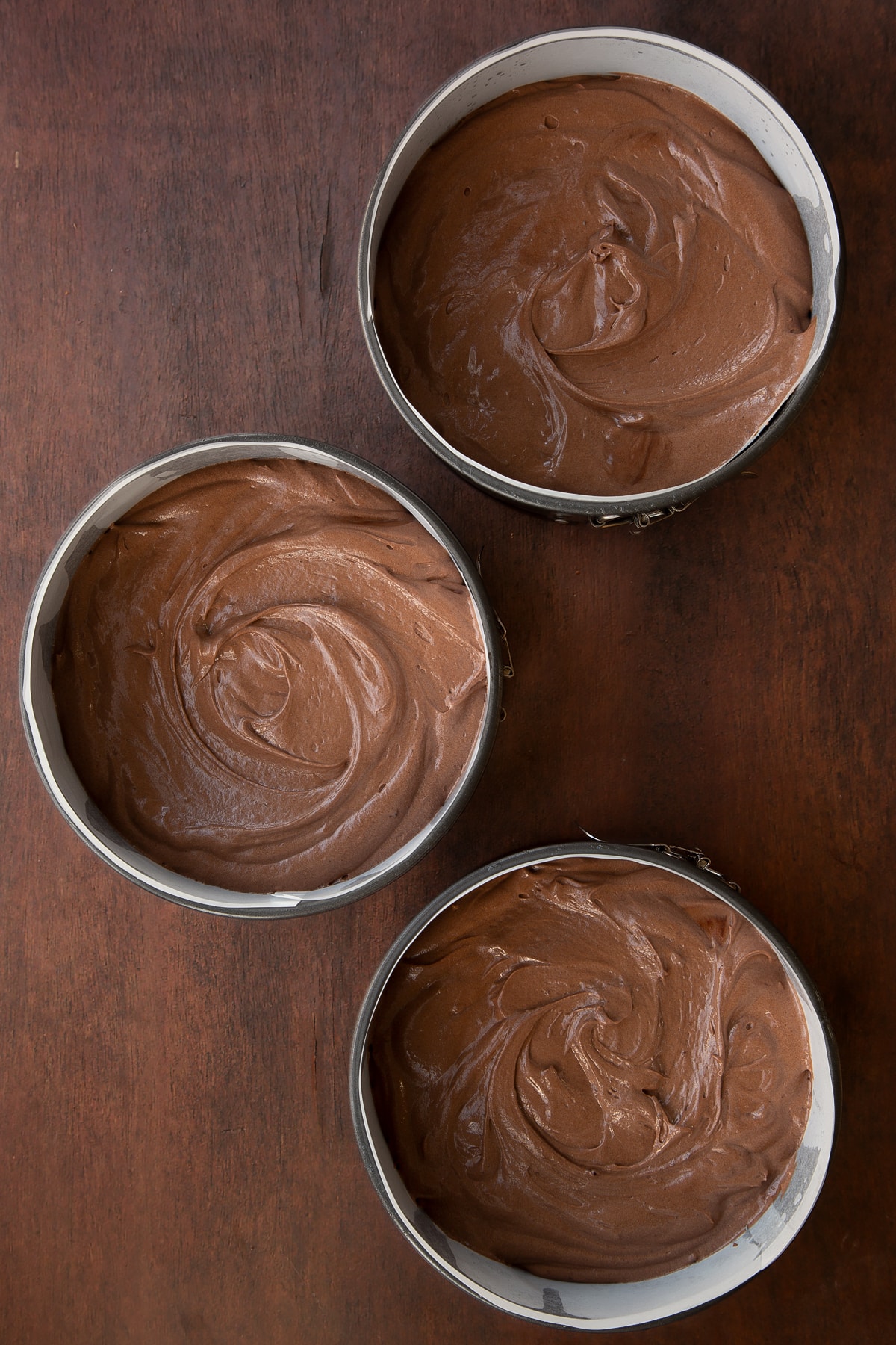 Chocolate Baileys cake batter in three lined cake tins.